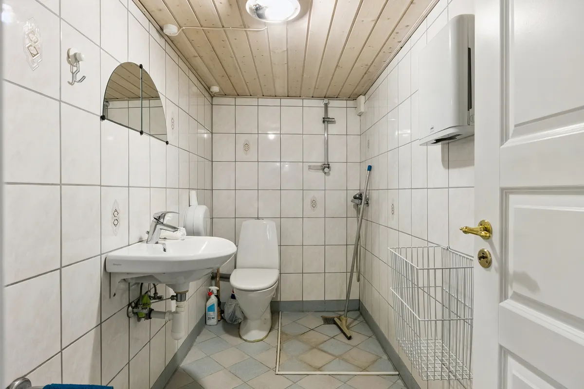 Et lille badeværelse med hvidt toilet, hvidt vasketøjsbord og hængende spejl. Der er et hængebliks håndklæde og en hængekrog med en hængekrog.