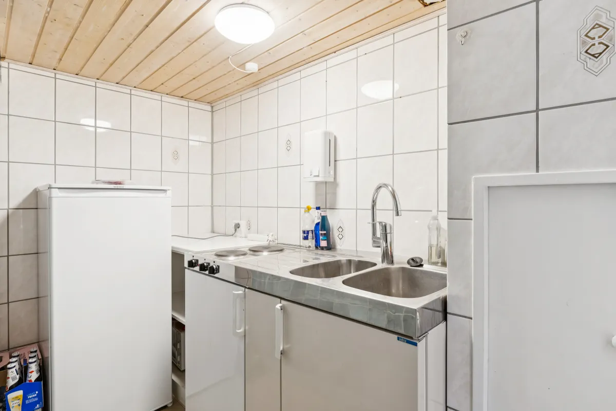 Alt-tekst: En rent holdt køkken med hvide vægge og loft, en indbygget komfur, en hvid køleskab og to lyse, runde, særegne lysekroner.