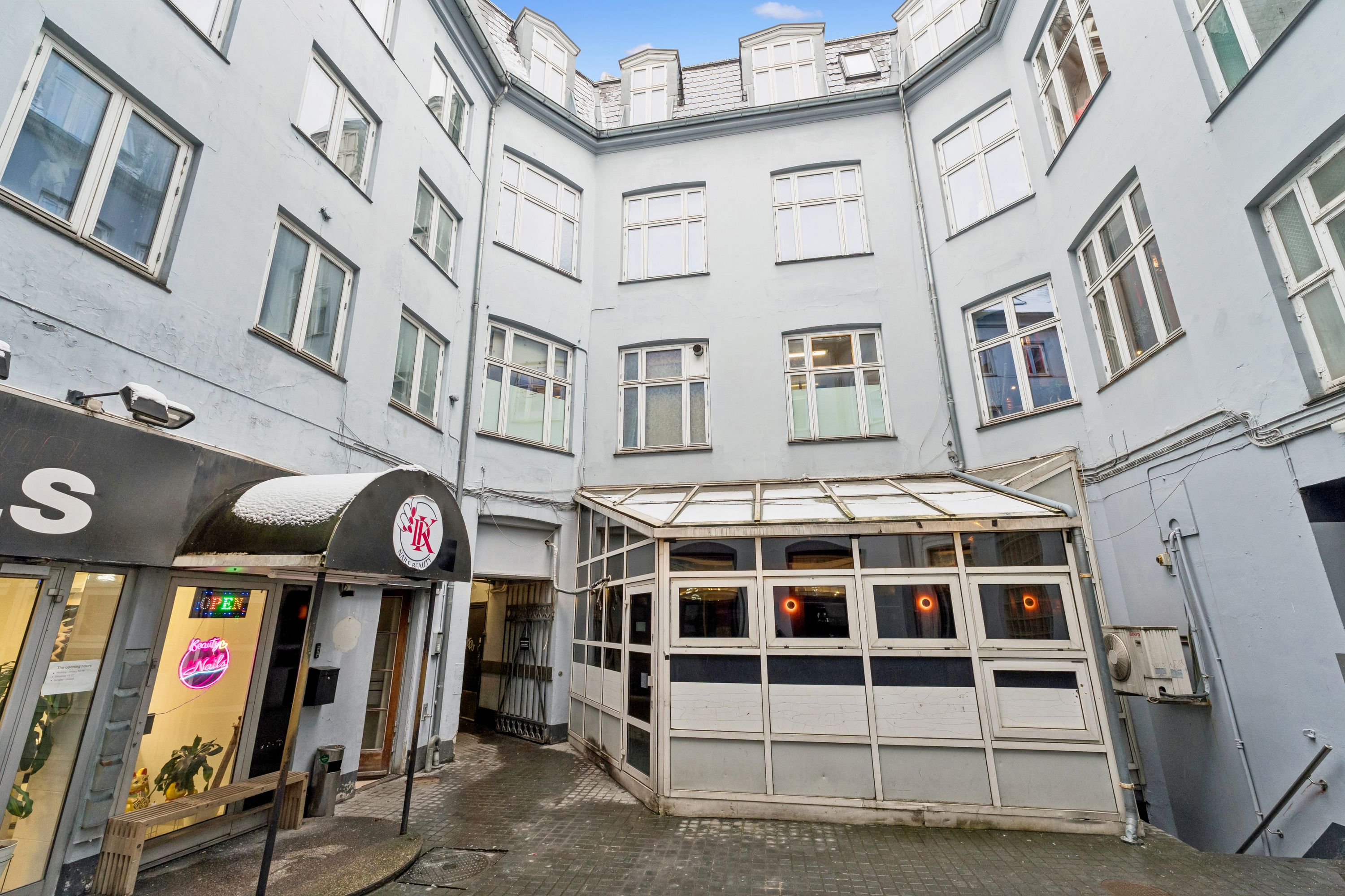 Kontor i bygning med mange vinduer og lyse gulve, køkken med dør og salgsvindue, glasdør til indgang, skur med vinduer og sne på taget