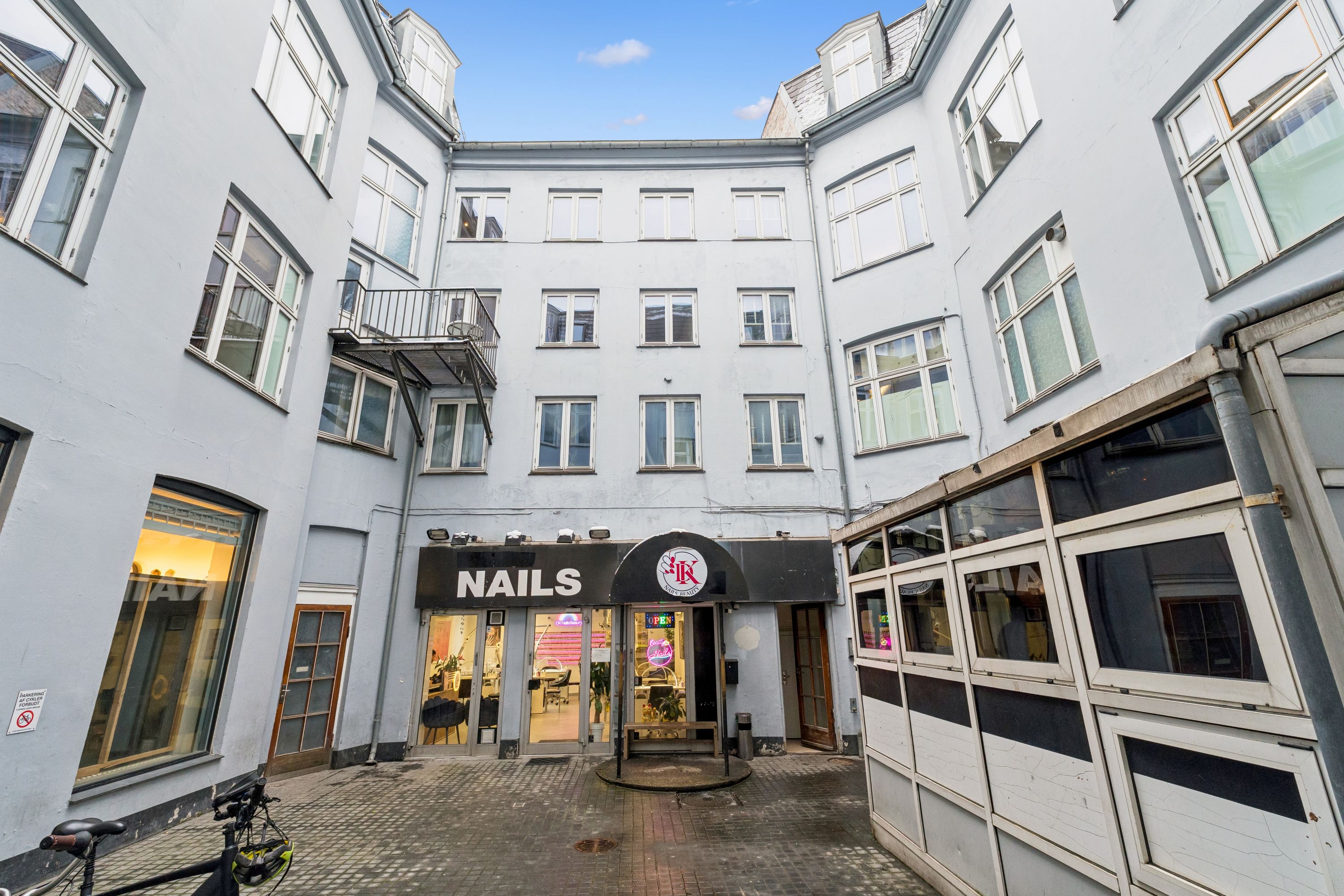 En cykel parkeret ved en kontordør med navnet Nails på facaden og et skilt med adgangstid og lukket i øjeblikket.