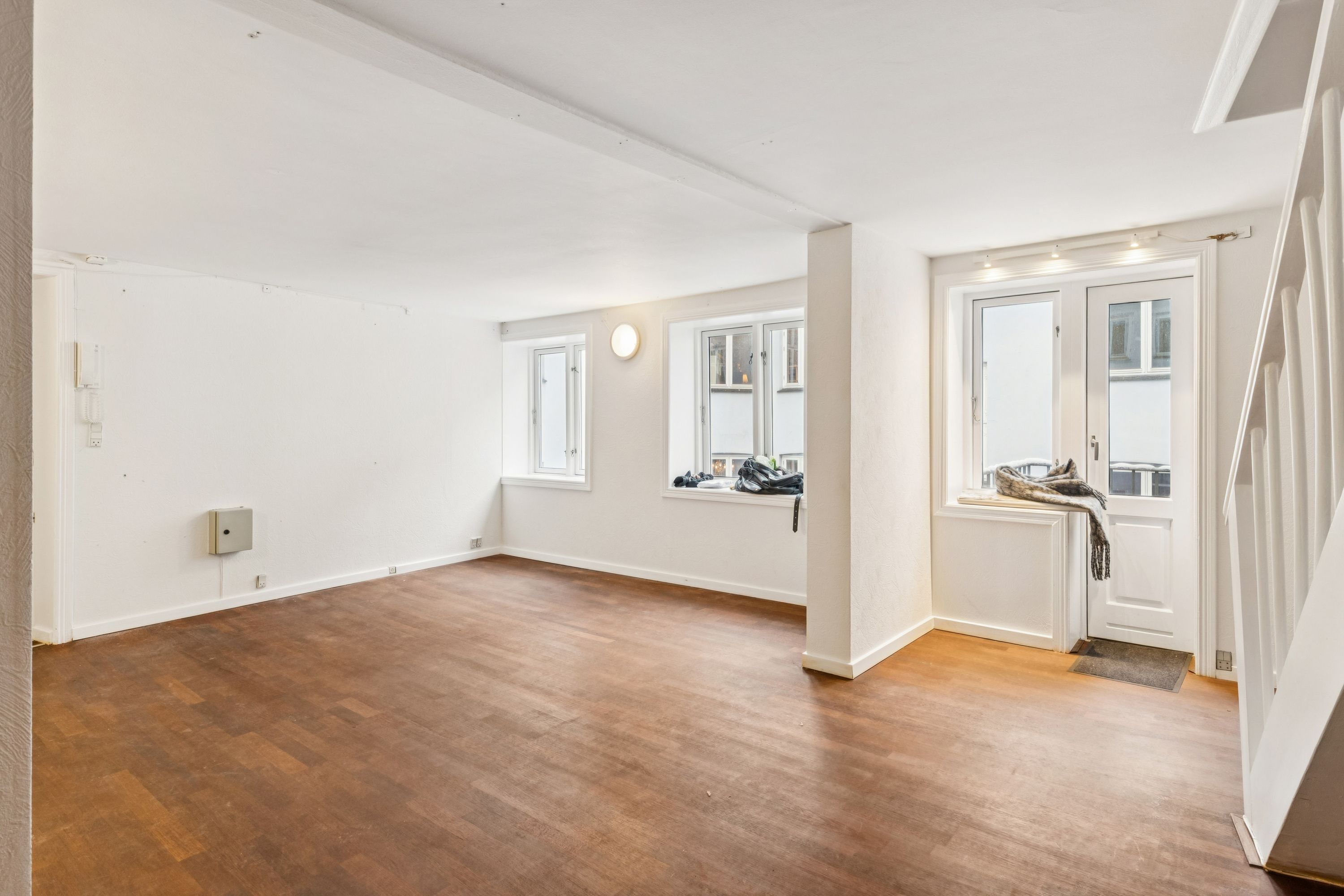 Kontor med lys og lyse gulve, åbne ruder og et vindue med et sølvfarvet ruderamme. Der er en hvid dør og en trappe med hvide sider.