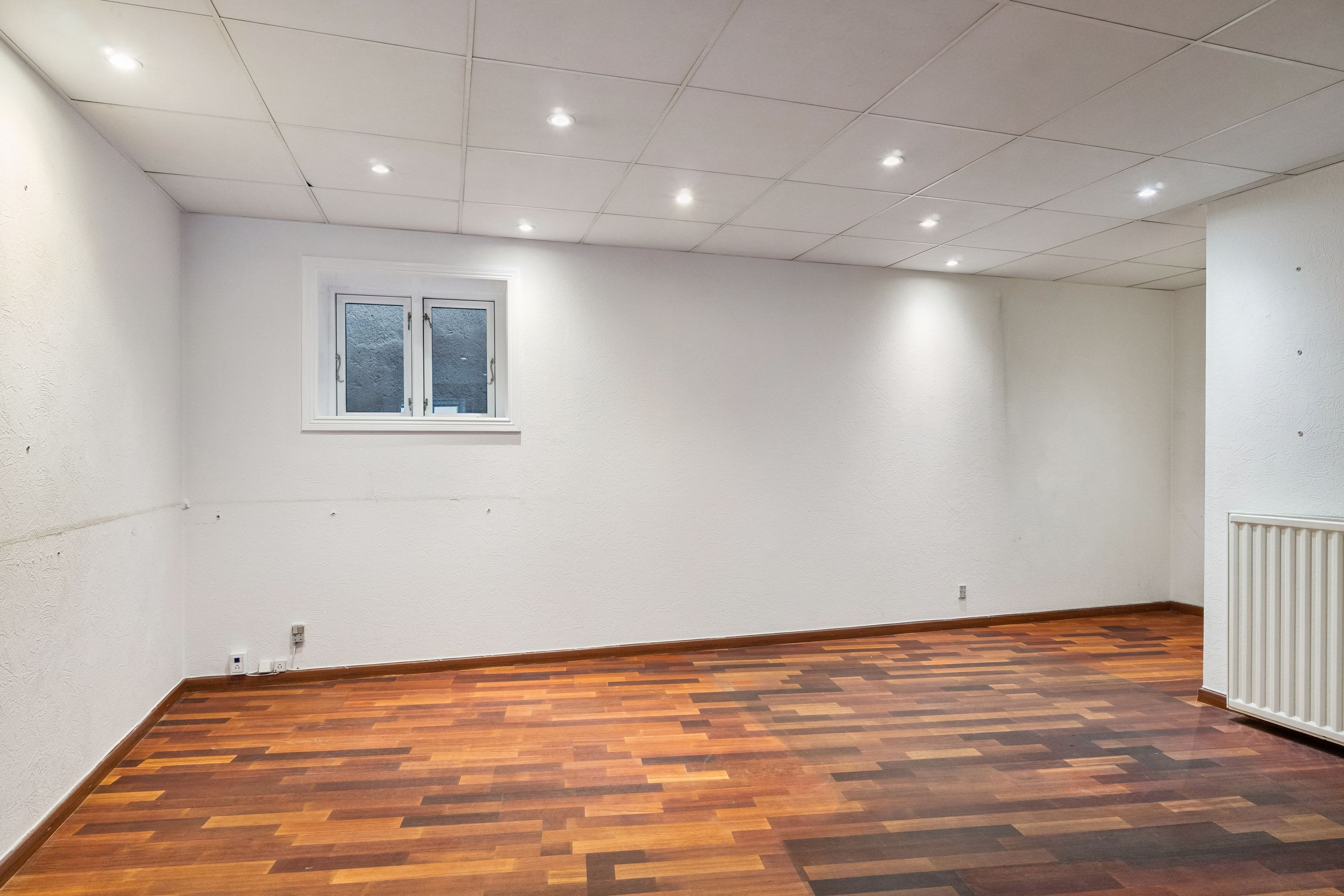 En tom kontor i København med lyse gulve og hvide vægge samt et vindue og radiator i højre side.