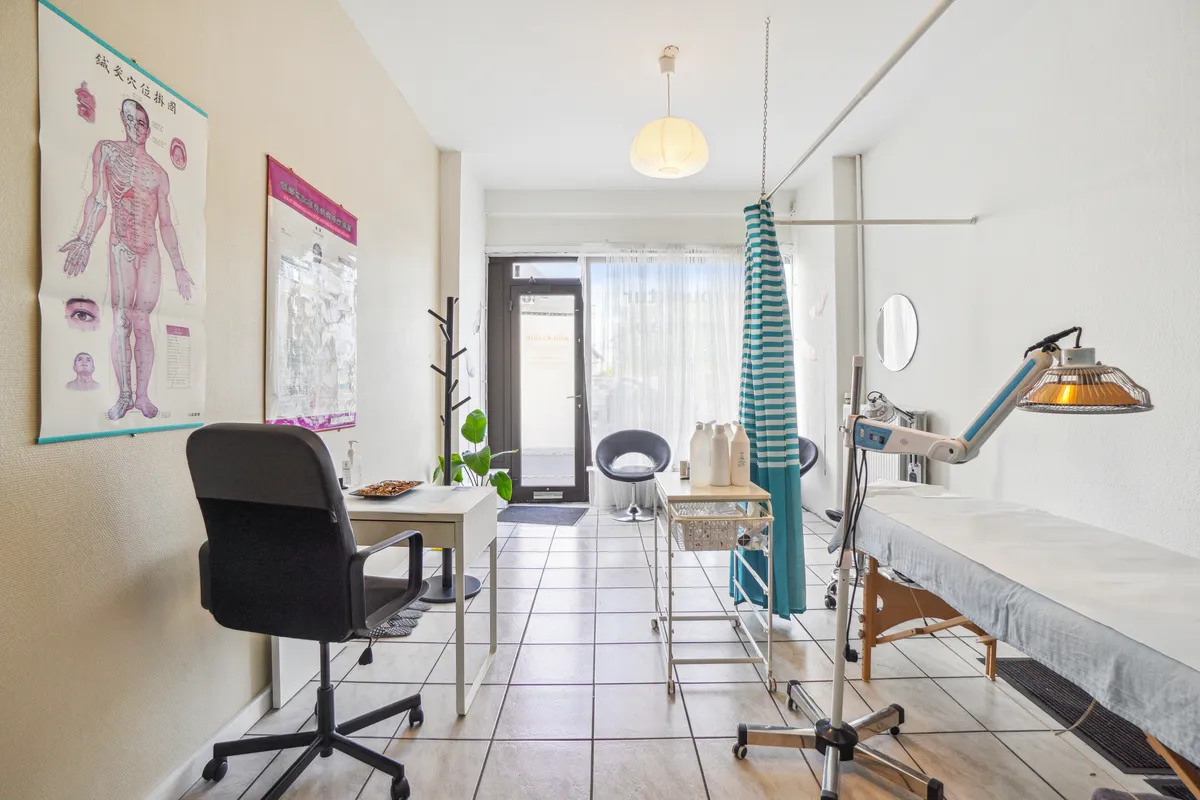 Lejlighedsmøbleret kontorplads med skrivebord, stol, lamper, tæppe og eksklusivt indretning. Planter og lysekroner til ekstra komfort. En stor åben dør og vinduer med gardiner.