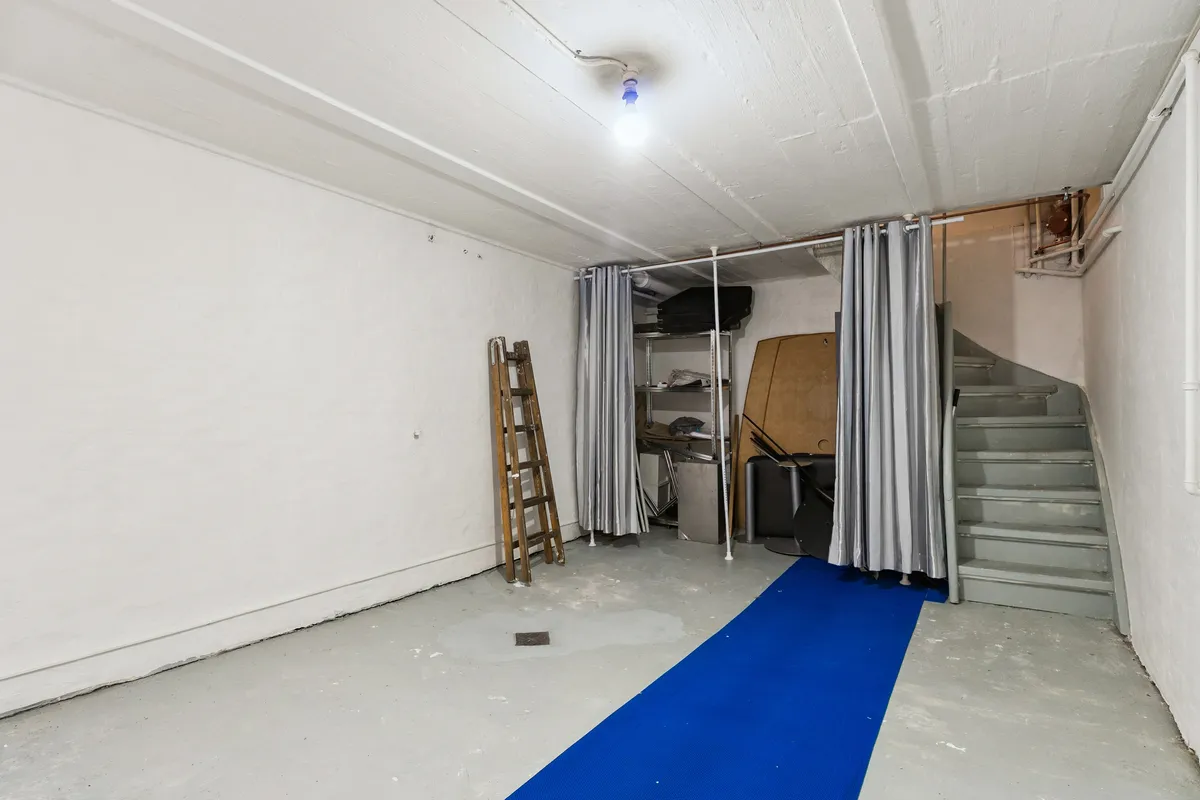 En lille butik med hvide vægge og loft samt et lyseblåt gulvtæppe i midten. Der er et stel, en stige og flere genstande i rummet.