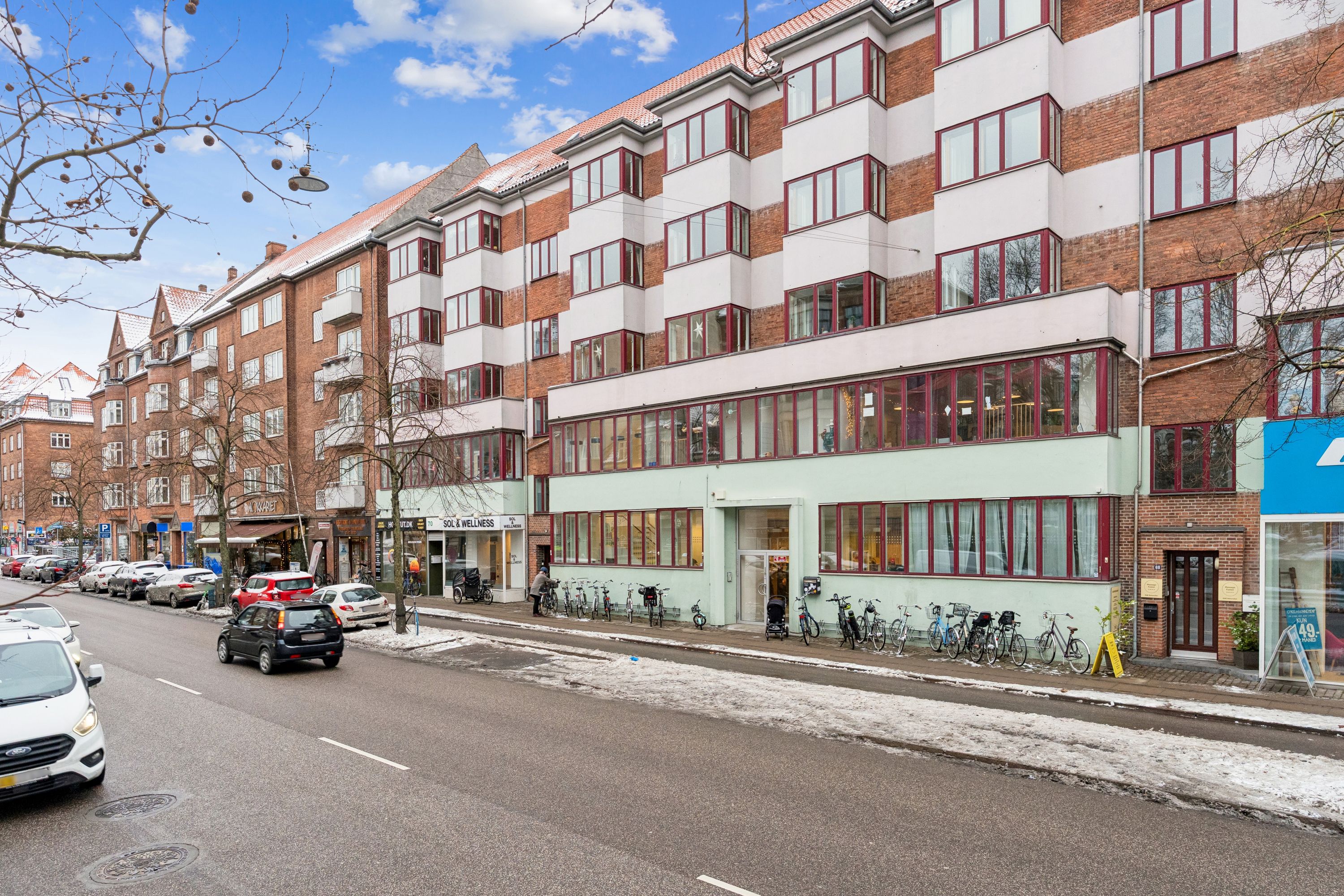 Butik med solcenter på Jagtvej 70, st. th, 2200 København N. Parkerede biler og cykler langs fortovet og sne på gaden.