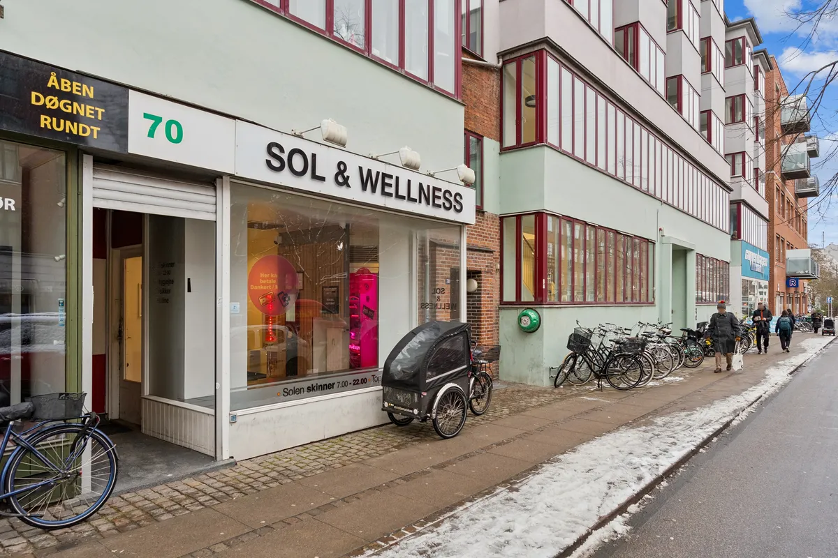 Sol & Wellness butik med stående sollampe og tre cykler udenfor på Jagtvej 70 i København. Adgangsvej og cykelparkering med folk og sne på siderne