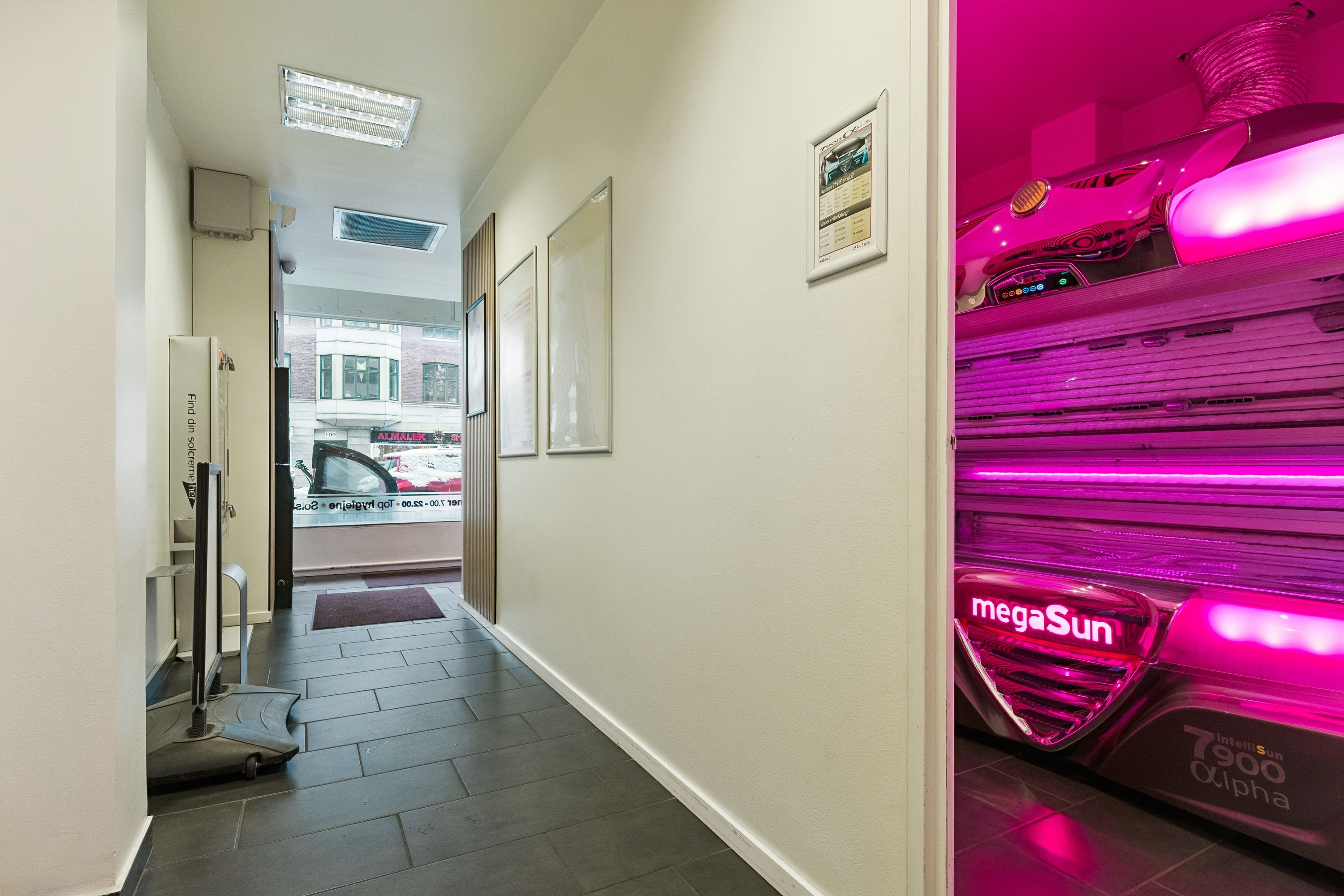 Solseng med lys rød belysning i en hvid klædt butik med fotoramme og skraldkurv. Fotoramme med solcenter-oplysninger. Også et gulv med gulvbelægning og gulve på gulvet.