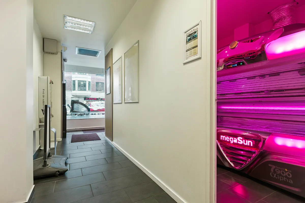 Solseng med lys rød belysning i en hvid klædt butik med fotoramme og skraldkurv. Fotoramme med solcenter-oplysninger. Også et gulv med gulvbelægning og gulve på gulvet.