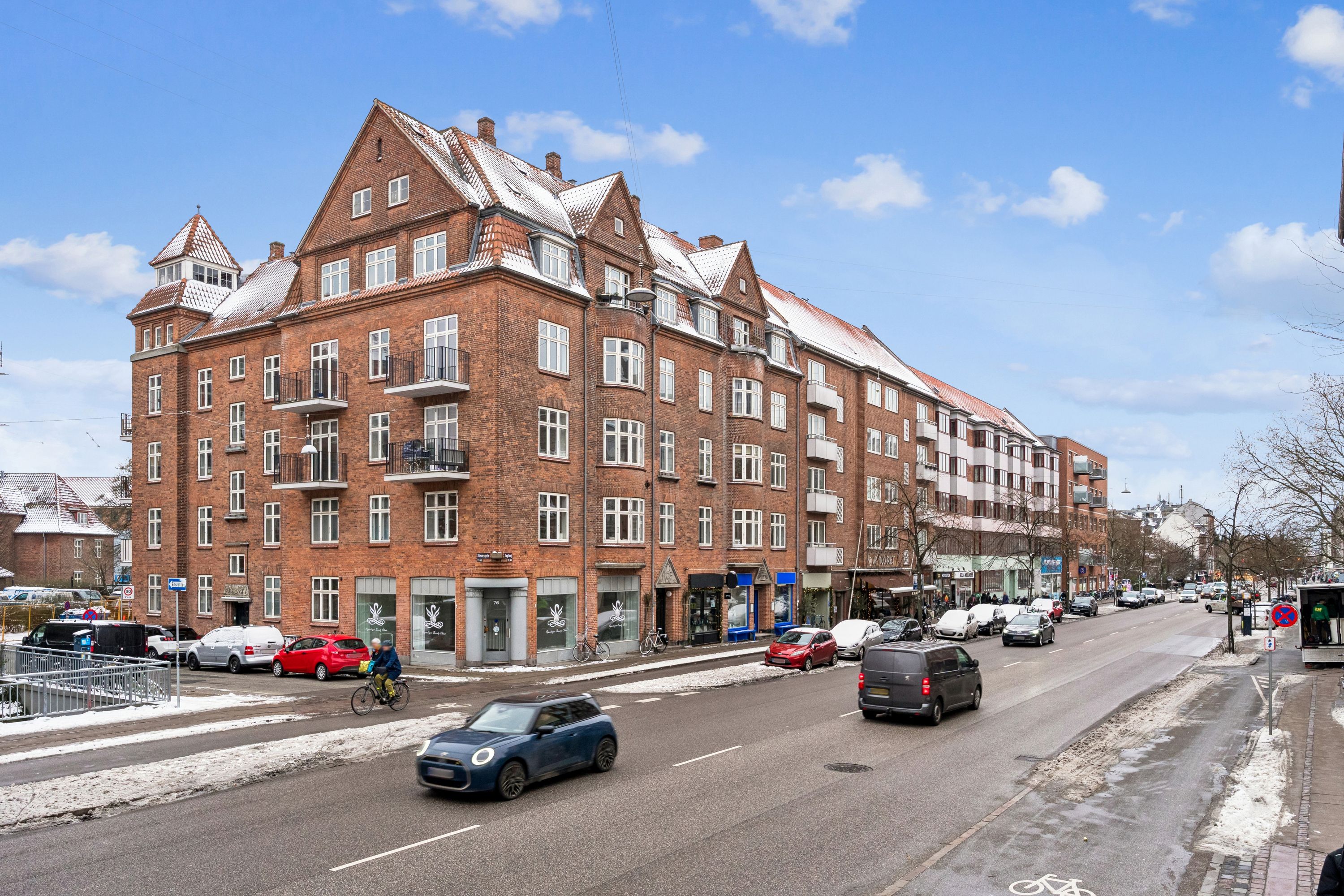 Menighedsbygning med røde mursten og hvide vinduerne i kvarteret Jagtvej, København. En cyklist kører på gaden, og biler parkeret foran bygningen