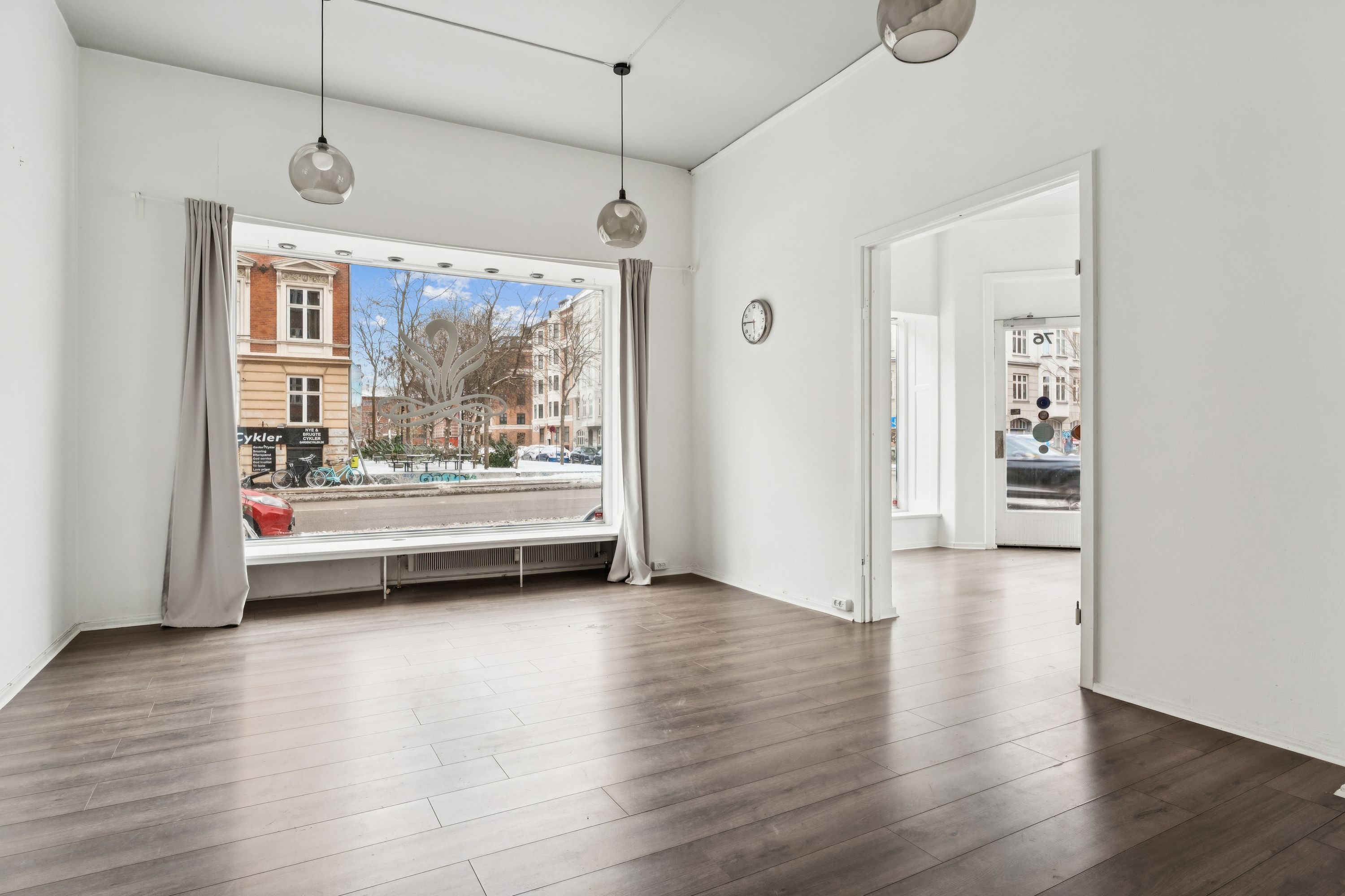 Lejlighed med glasvinduer og åbne døre mod Jagtvej 76. Indvendigt ser gulvet og væggene pænt ud. Loftet er dekoreret med to lysekroner og en klokkeskærm.