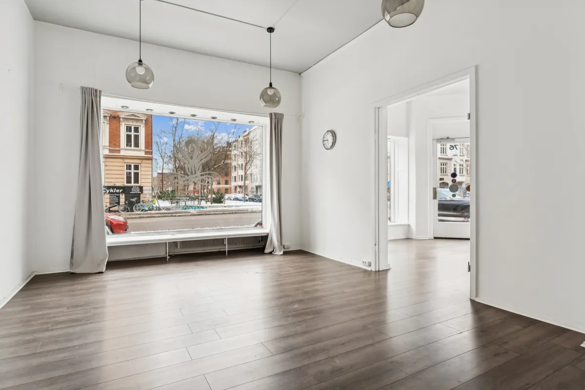 Lejlighed med glasvinduer og åbne døre mod Jagtvej 76. Indvendigt ser gulvet og væggene pænt ud. Loftet er dekoreret med to lysekroner og en klokkeskærm.
