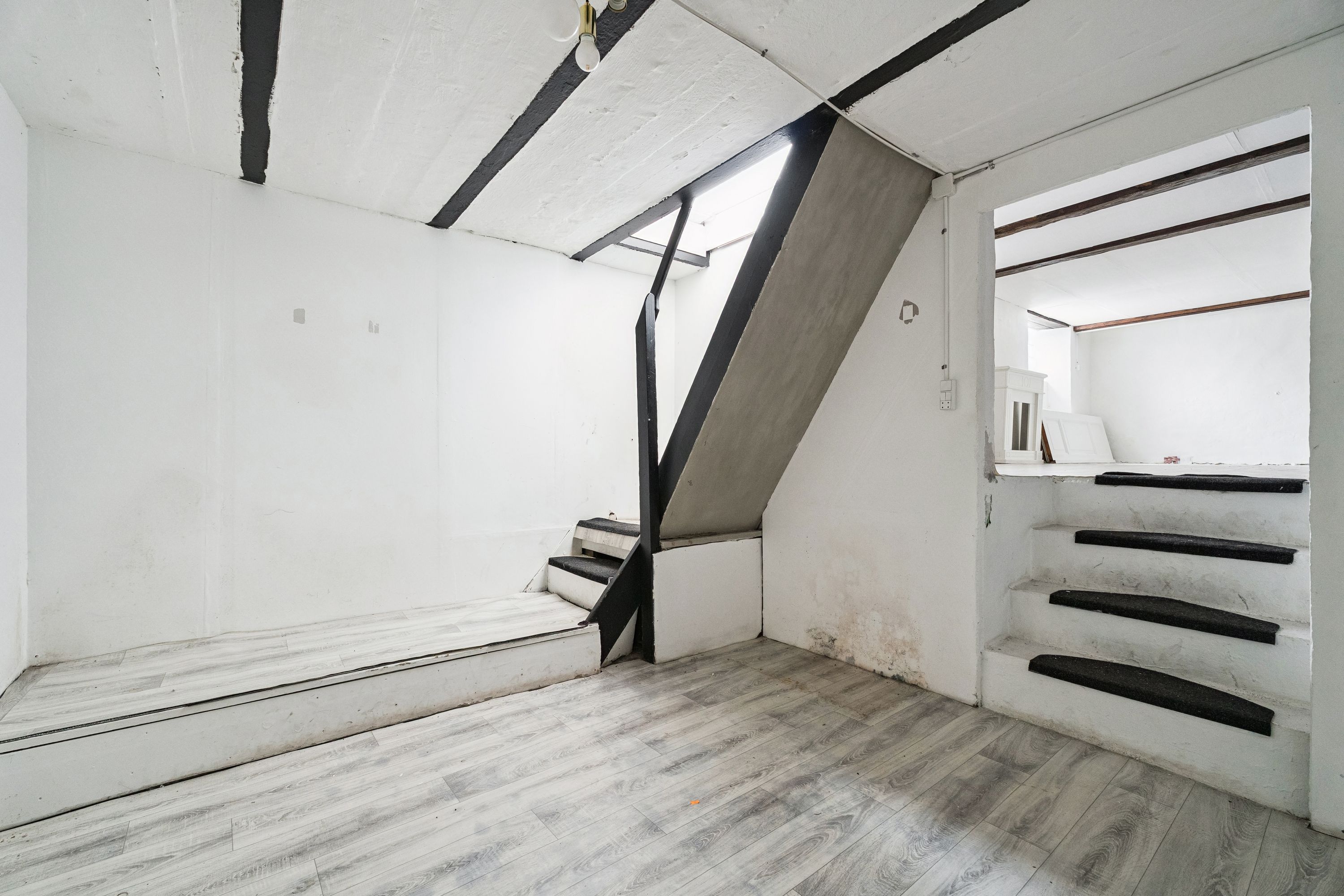 Et nyt vindue og lyse trapper er synlige i det hvide rum med gulvbelægning, og der er også en trappe op til en anden etage