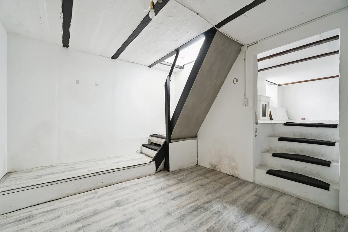 Et nyt vindue og lyse trapper er synlige i det hvide rum med gulvbelægning, og der er også en trappe op til en anden etage