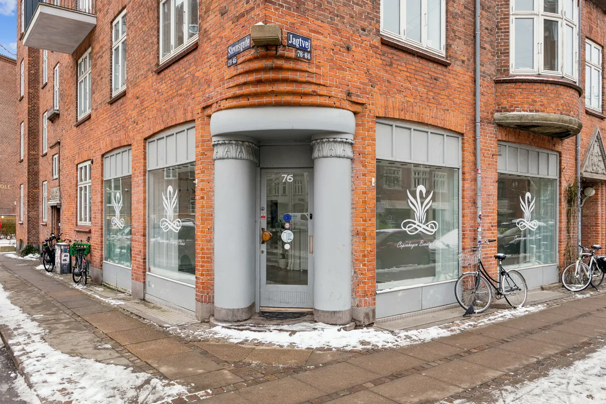 Butik i København med glasruder, logo, og nummer 76 på Jagtvej, med sne og cykler på fortovet og røde mursten.