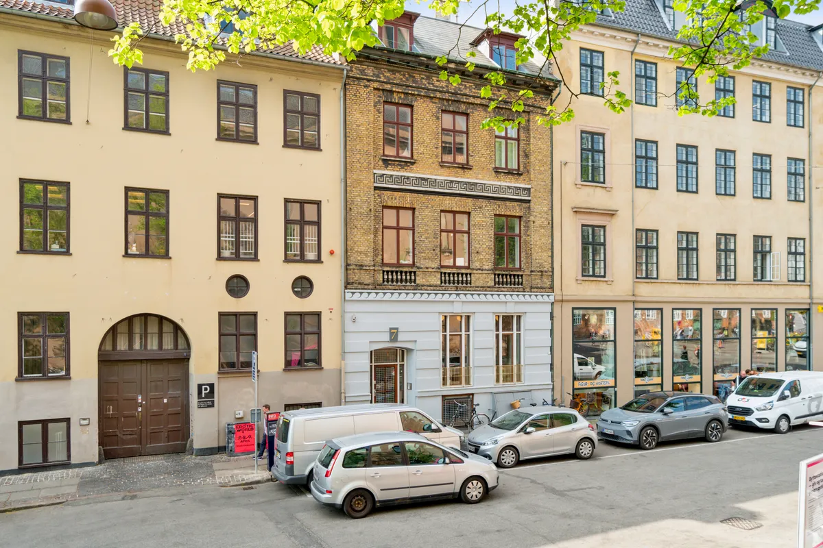 Kontorbyggeri med tre biler parkeret imod fortovet og en mand iført en hvid skjorte og bukser står udenfor