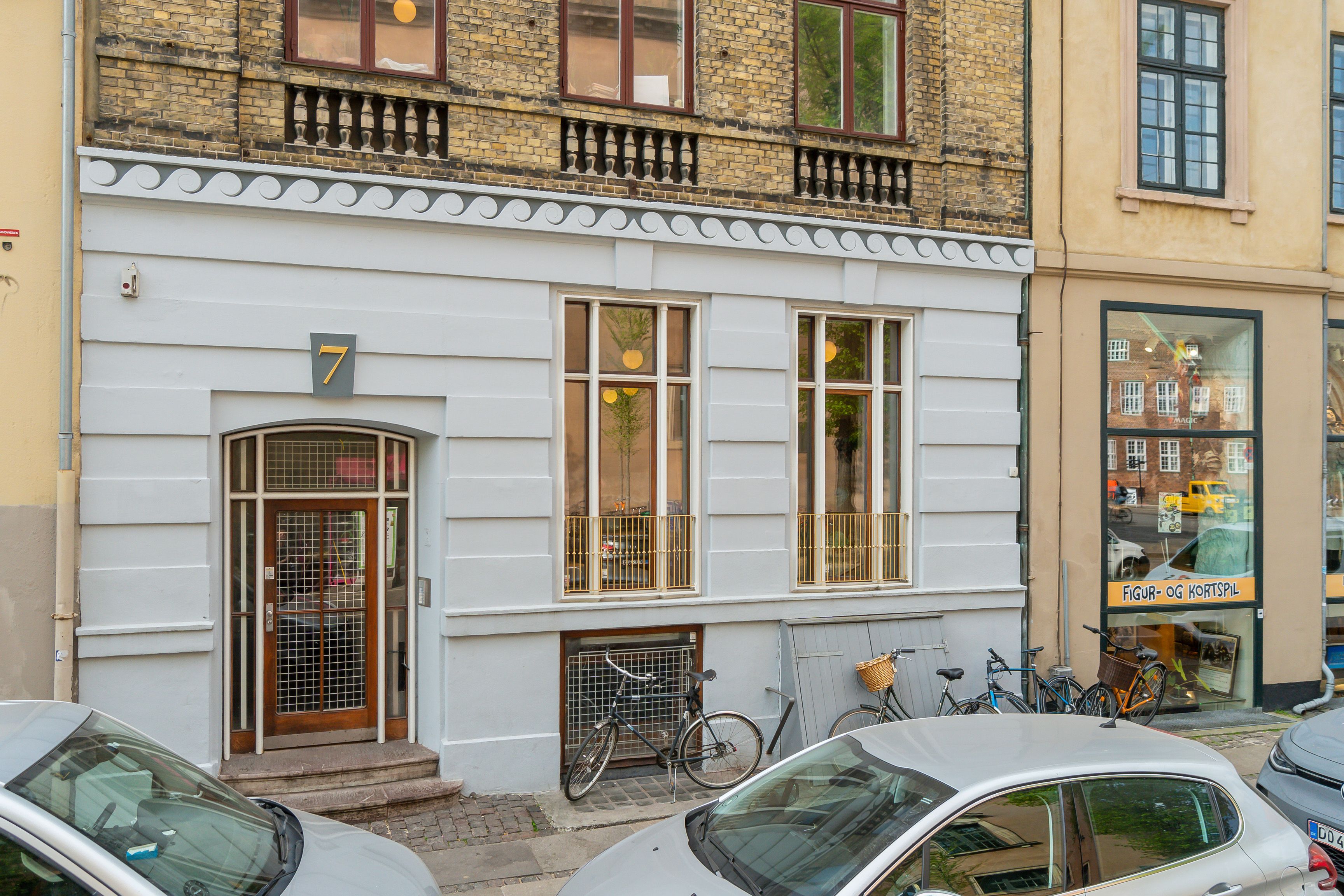 Kontor på Dyrkøb 7 i København K. Lejlighed med tre vinduer og indgang. Fire cykler står parkeret uden for. To biler parkeret uden for bygningen.