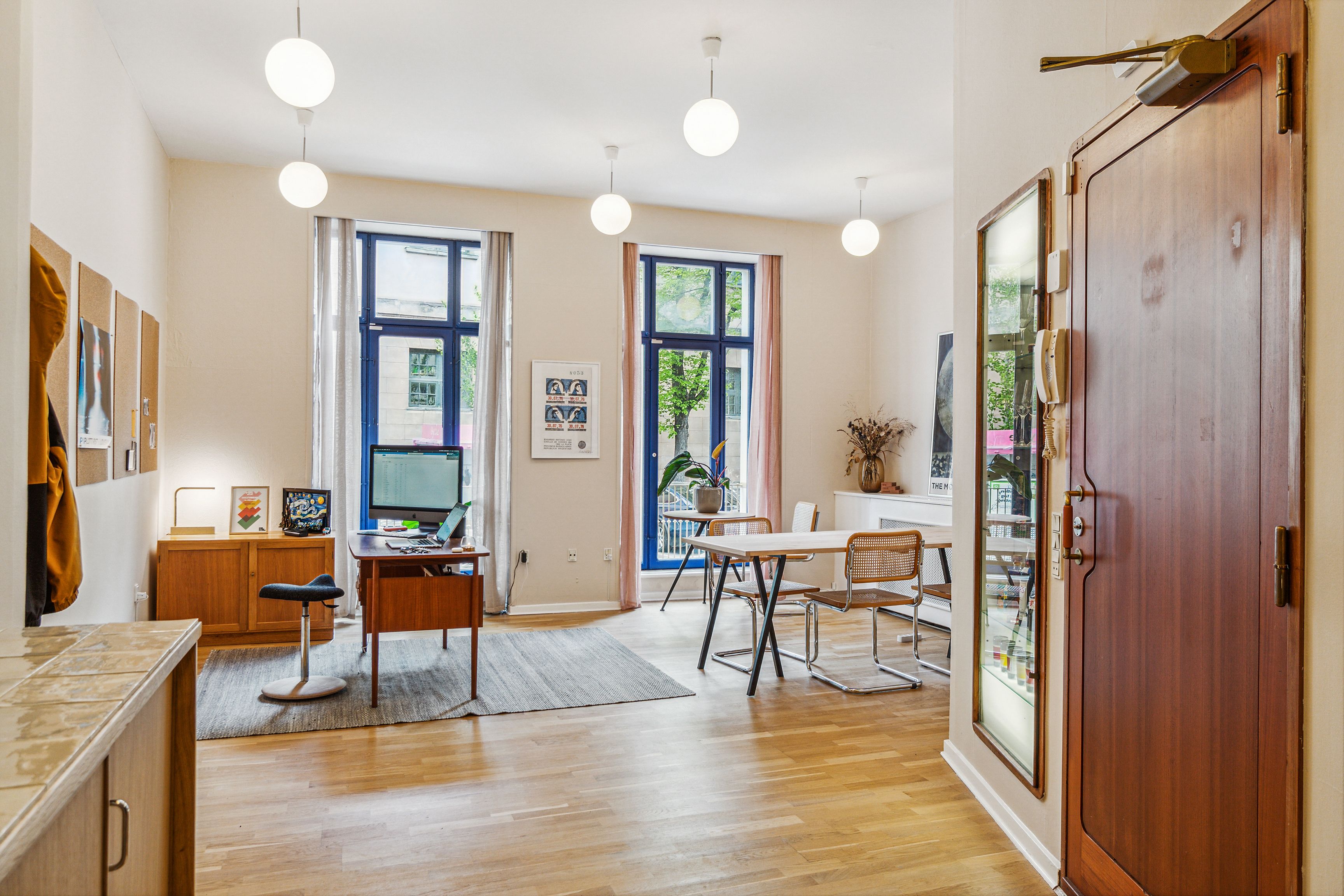 Kontor med lyse gulvbelægning, skrivebord og computer samt moderne møbler og vinduer med udsigt til gade.