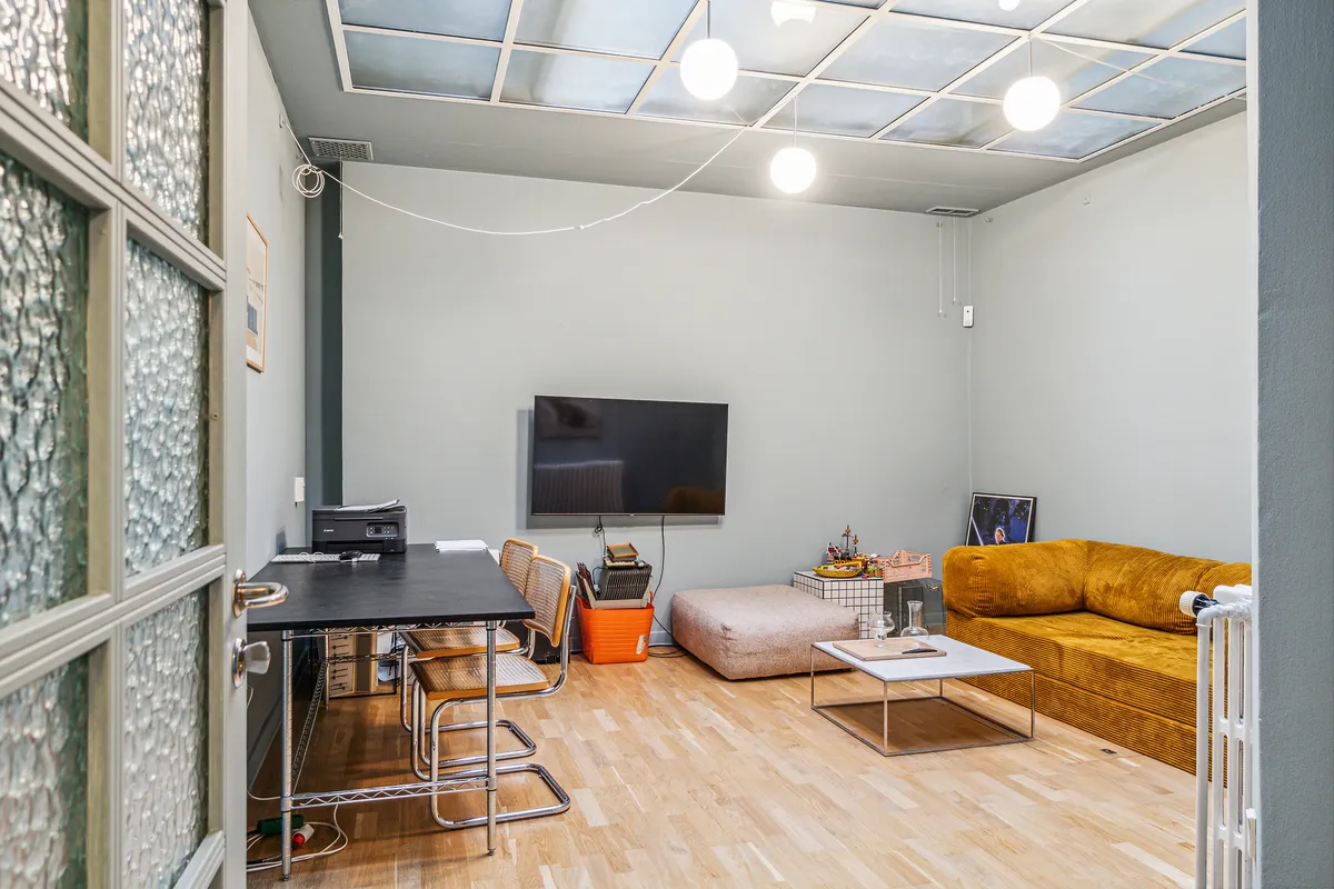 Kontor med veludstyret arbejdsområde og skrivebord med printer samt en fjernsynsskærm og et sofabord med sofa.