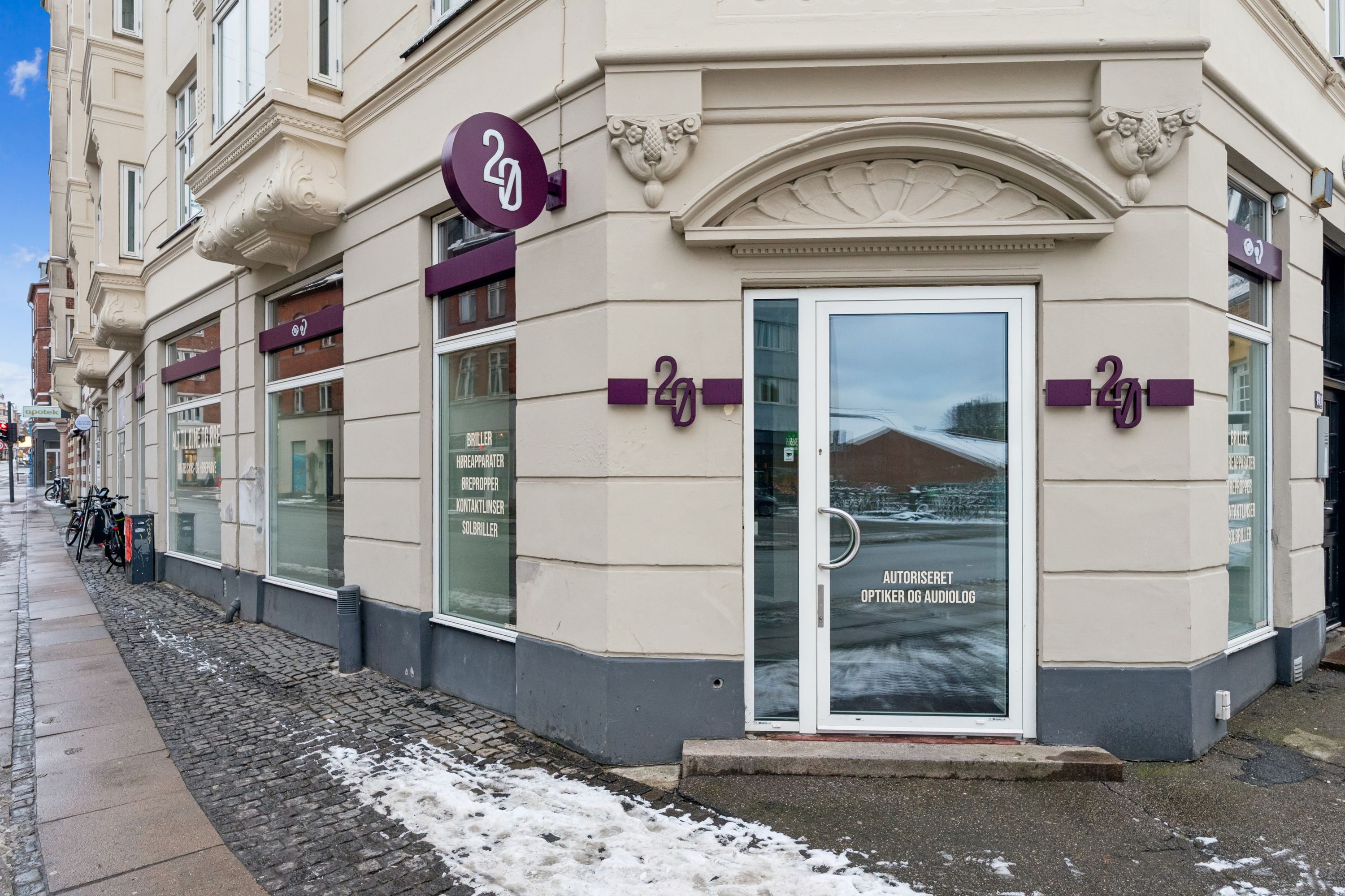 Valby Langgade 49B butik med teksten "Autorisert Optiker og Audiolog" og store glasruder, snødækket fortov og gadebelysning