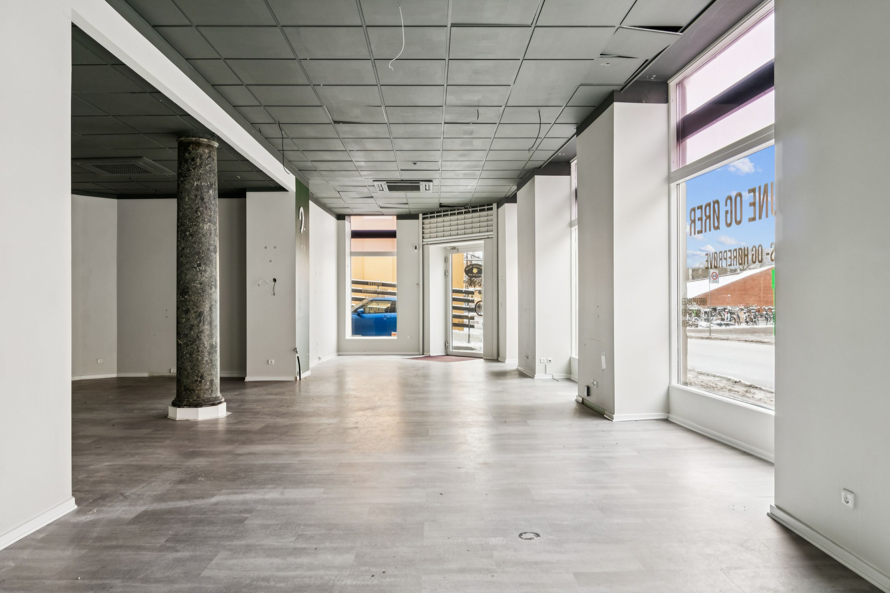 Markant hjørnebutik med tomme vægge, moderne gulv og en stor glasdør, der vender ud mod Valby Langgade. En søjle og lyseloft udgør det grafiske design