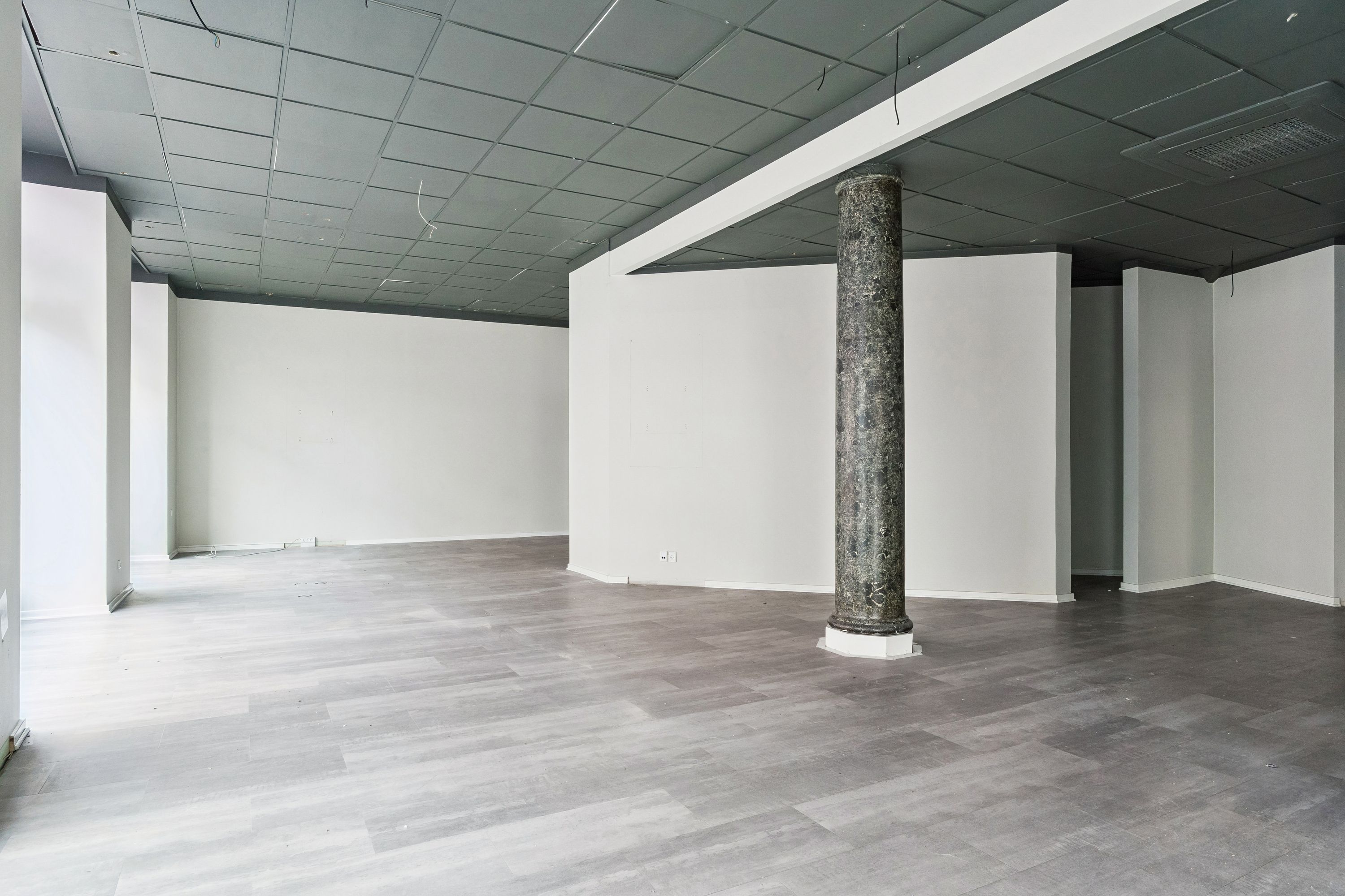 En stor, tom hjørnebutik med højt loft og marmorsøjle, lysegrå gulvbelægning, og hvide vægge på Valby Langgade 49B, st., i området ved Tingstedet.
