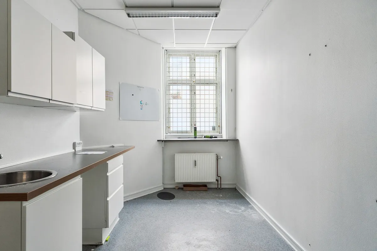 En tom hjørnekontor med hvide vægge, en vinduesbank med radiator, og et hvidt tavle, der er fastgjort til væggen og en ren gulvoverflade