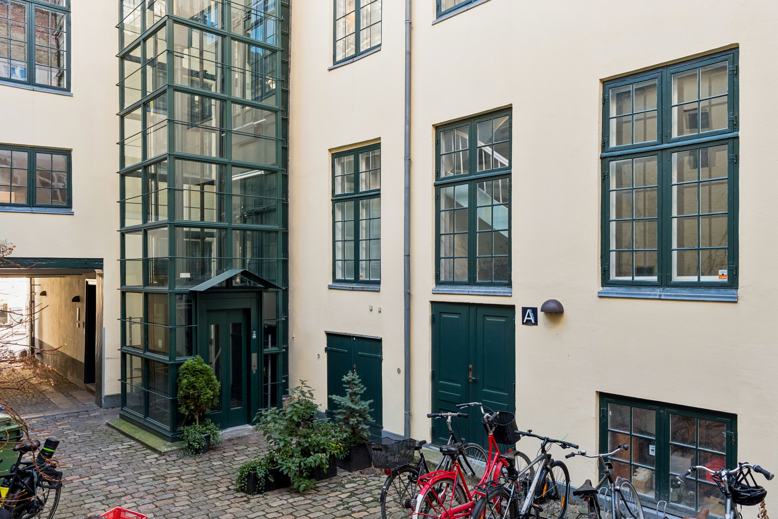 Kontor til leje i København med grønne vinduer, glasdøre og parkerede cykler i forgrunden samt en lysegul facade med mørkeglasruder