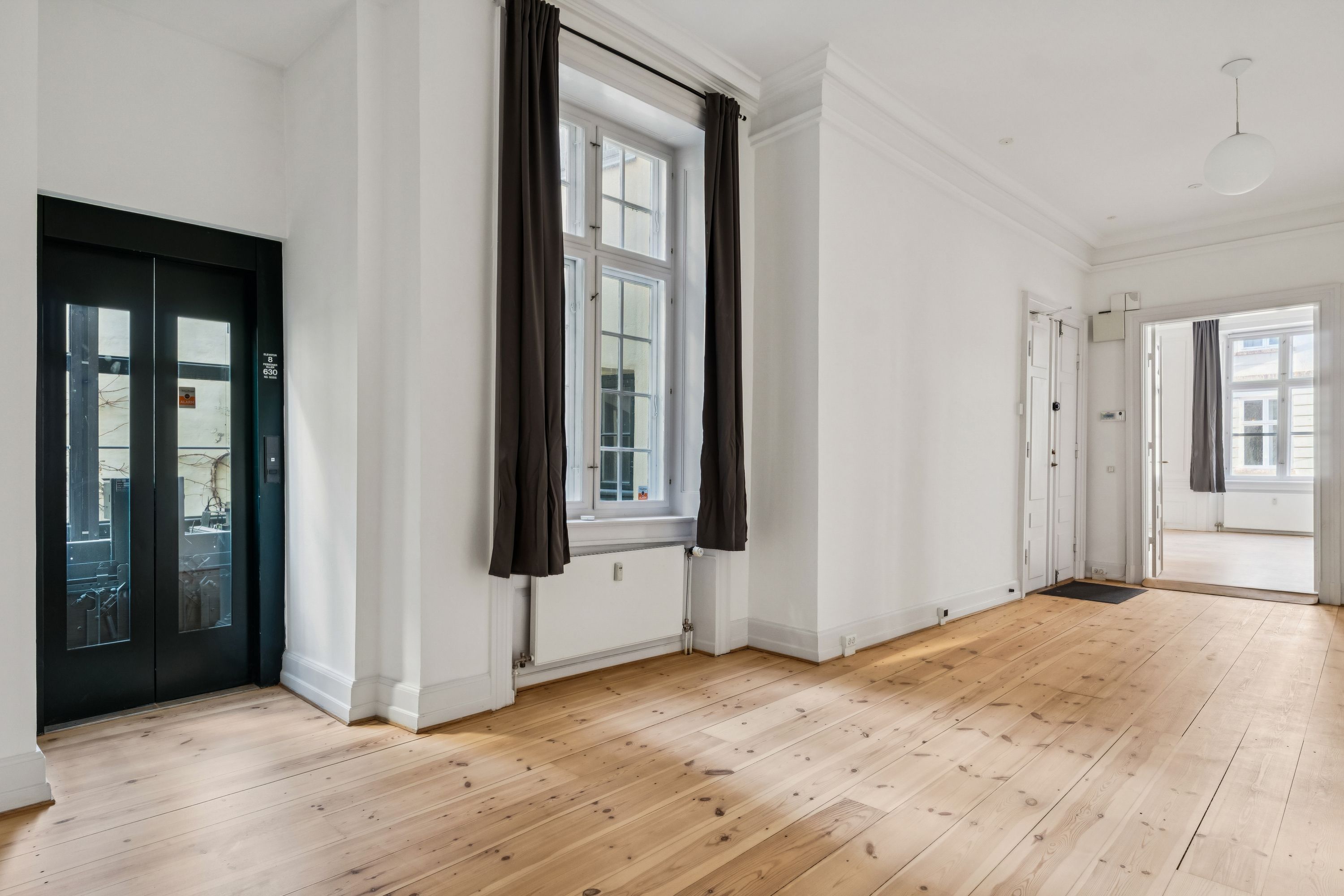 Hjørnelokaler med lyse og rummelige værelser, hvide vægge, lyse trægulve og store vinduer med gardiner samt to separate indgange og lysekroner