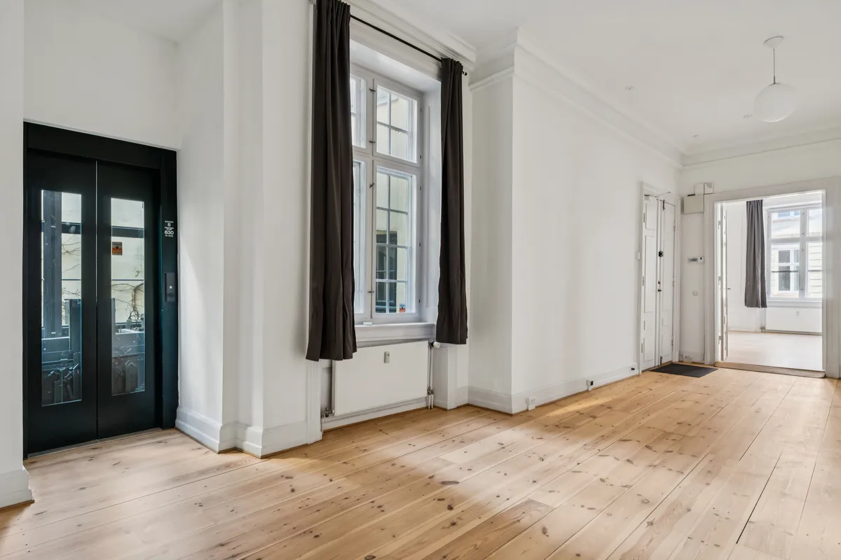 Hjørnelokaler med lyse og rummelige værelser, hvide vægge, lyse trægulve og store vinduer med gardiner samt to separate indgange og lysekroner