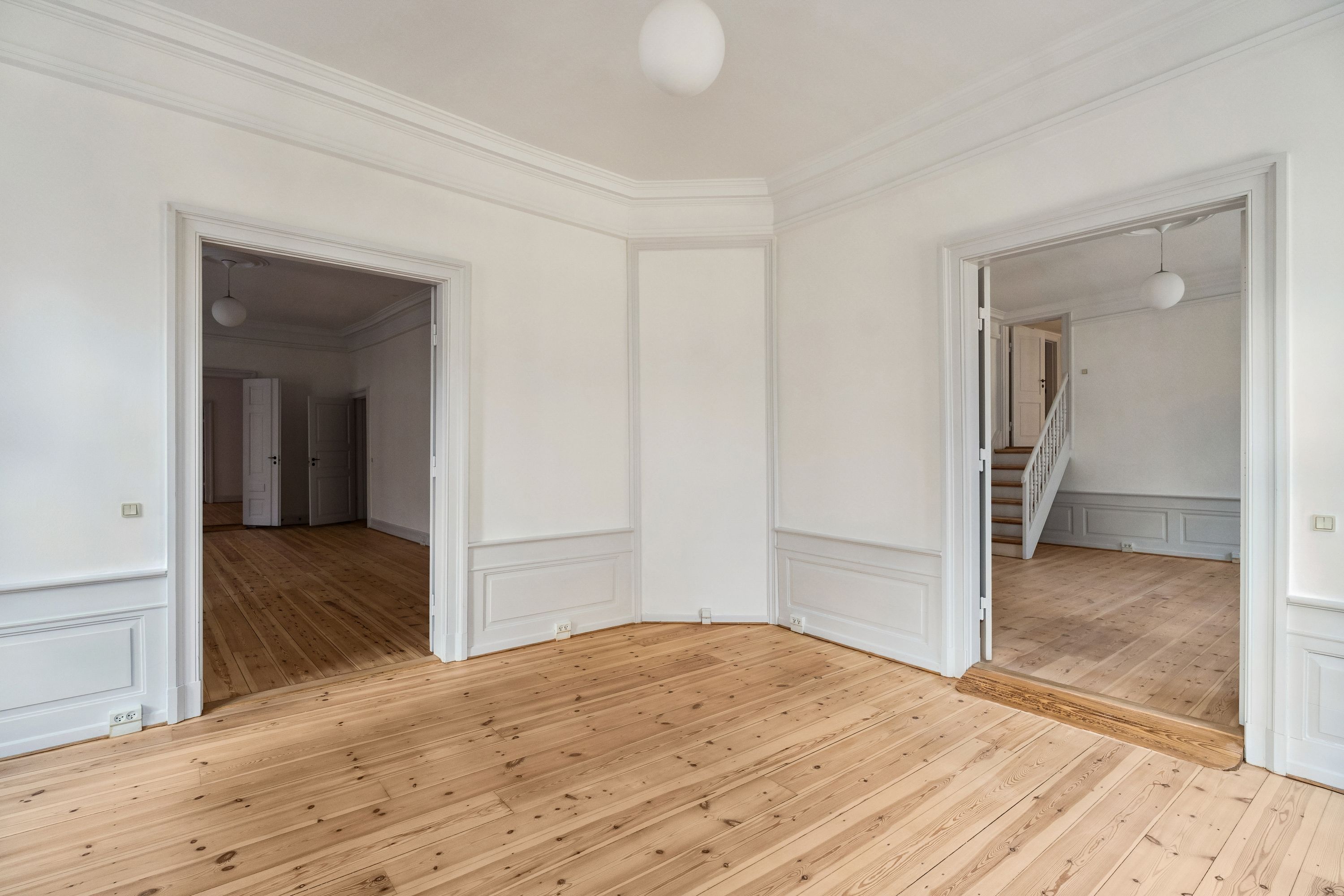 Et rummeligt, lyse og stilfuldt kontorrum med lyse trægulve og hvide vægge. Et stort gulvspejl og lyse pærelampen i loftet giver et eksklusivt og luksuriøst look