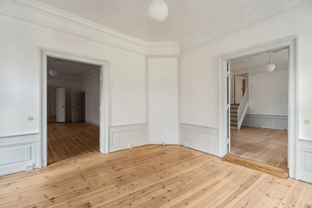 Et rummeligt, lyse og stilfuldt kontorrum med lyse trægulve og hvide vægge. Et stort gulvspejl og lyse pærelampen i loftet giver et eksklusivt og luksuriøst look