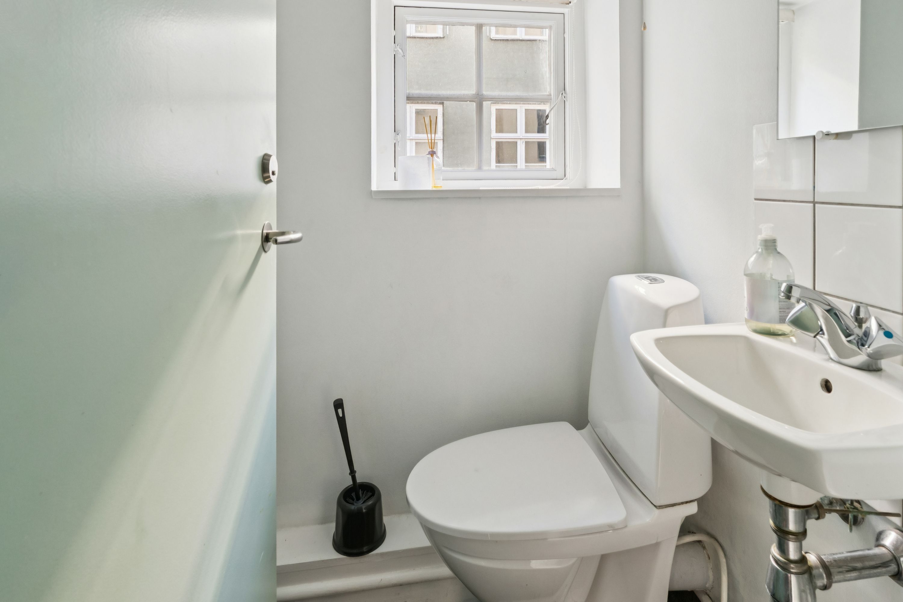 En lille, rent holdt badeværelse med hvid toilet, hvid vask og en sæbeflaske ved vandhanen