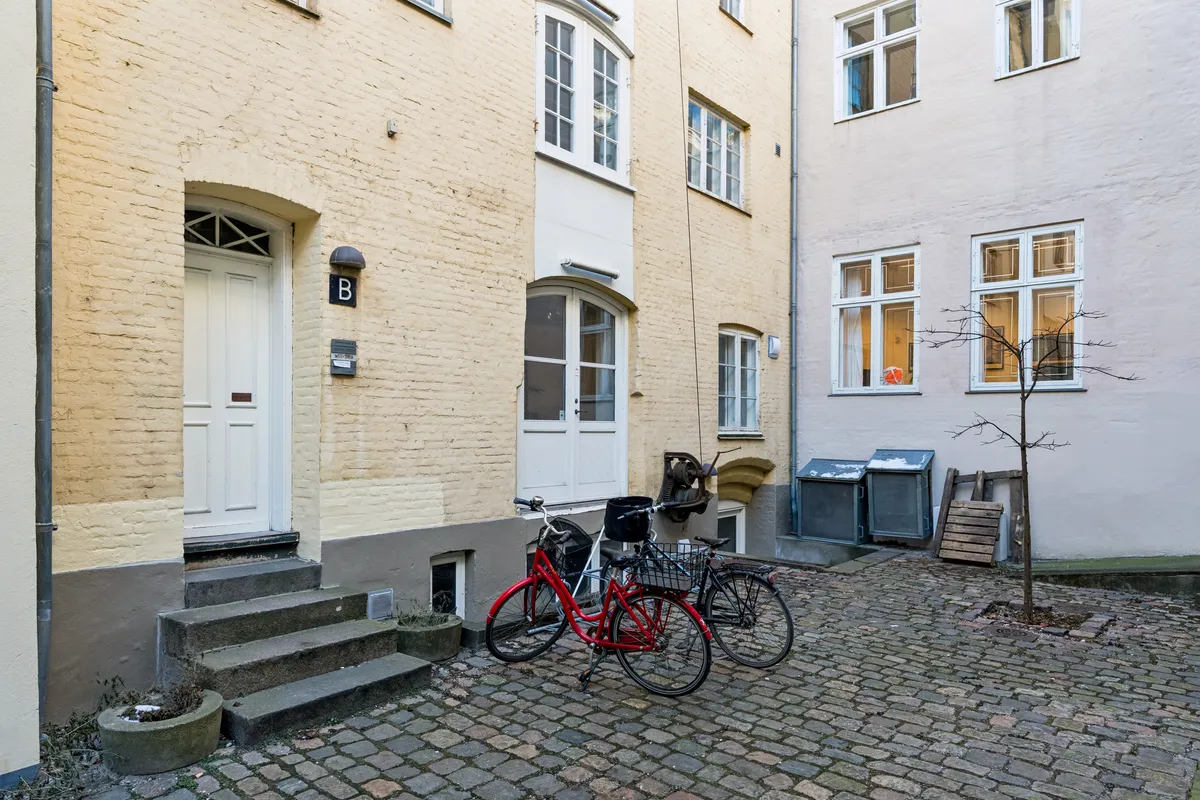 Rådhusstræde 6B er en charmerende og velindrettet lejlighed i København. Rød cykel og to hvide døre. Gul og hvid mursten og moderne vinduer.
