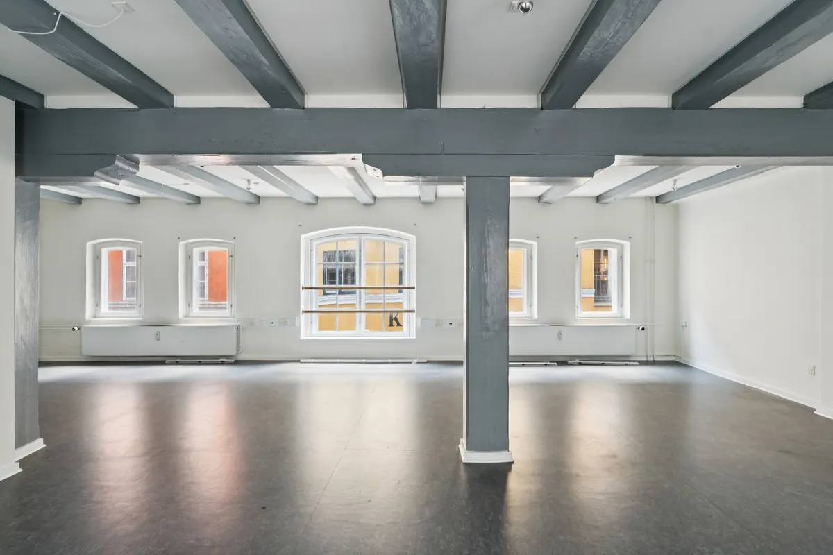 Rådhusstræde 6B, København K, kontorlokaler med højloft, tre store vinduer, moderne gulvbelægning og lyse vægge. En stor søjle i midten af lokalet.