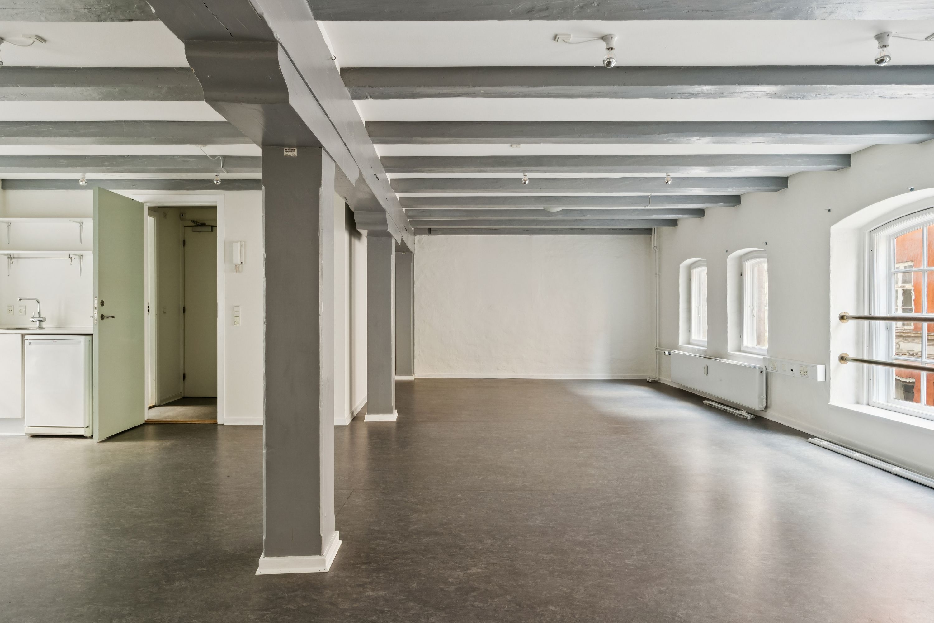 Indvendigt i det lyse og rummelige kontor er der lysegrå søjler og bjælker, lysegule vægge og moderne vinduer. Der er en åben dør til køkkenet med lysegrå hjørnehylder og en hvid ovn