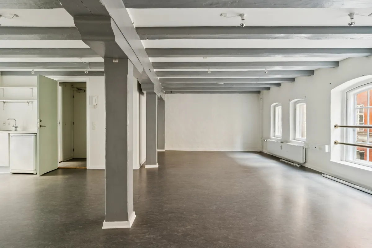 Indvendigt i det lyse og rummelige kontor er der lysegrå søjler og bjælker, lysegule vægge og moderne vinduer. Der er en åben dør til køkkenet med lysegrå hjørnehylder og en hvid ovn
