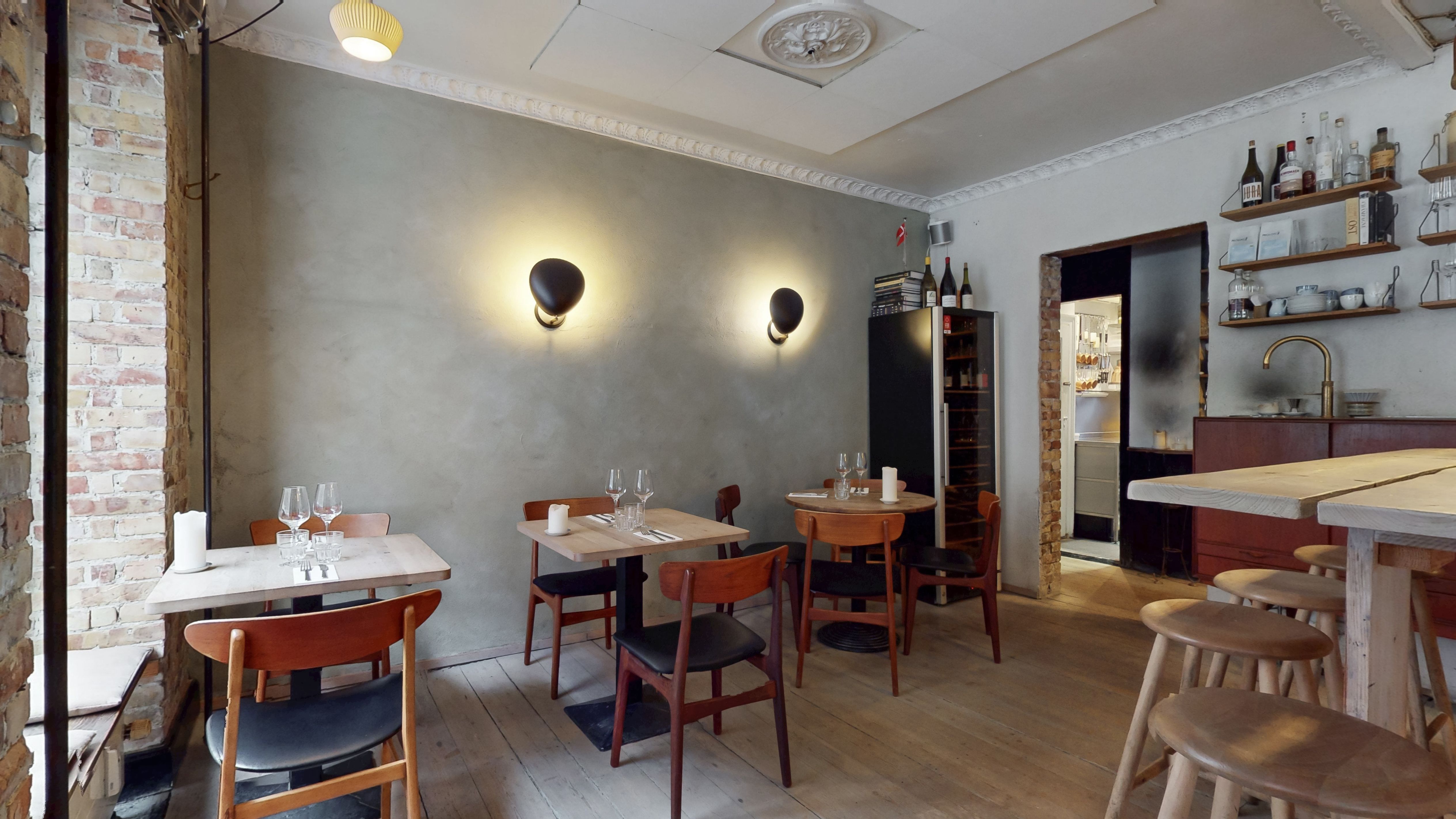 Restaurant med lyse træborde og stole med mørke læderpuder samt lyse loftslamper og en gulv af træ