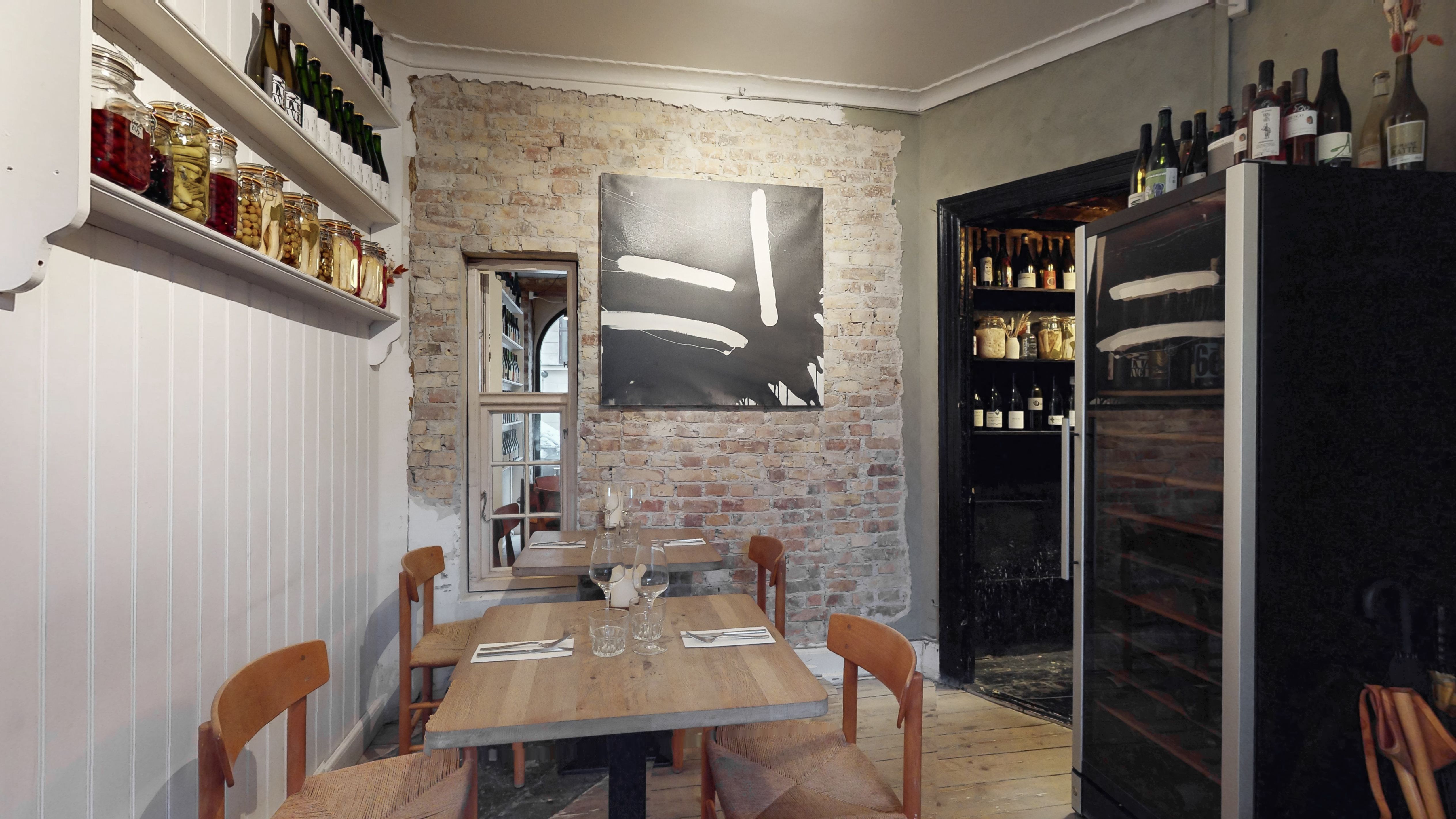 Et lille bord med fire stole og en flaske og glas i baggrunden og et køleskab med flere vinflasker