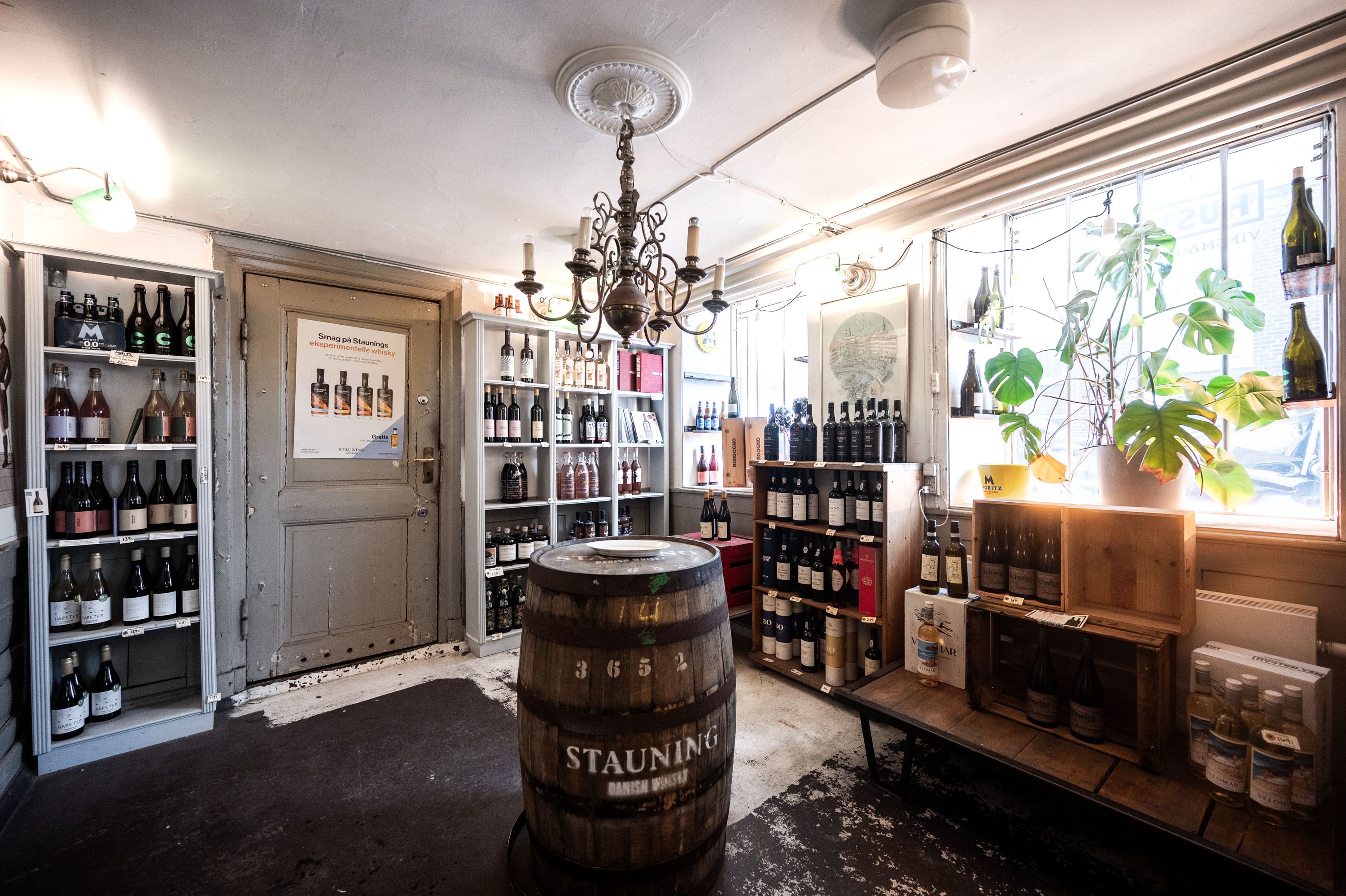 Historisk butikslejemål med vin og øl i Naboløs, få skridt fra Gammel Strand. Værelser med vinflasker, ølflasker, champagneflasker, plante og lysekroner.