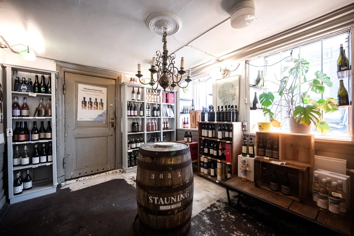 Historisk butikslejemål med vin og øl i Naboløs, få skridt fra Gammel Strand. Værelser med vinflasker, ølflasker, champagneflasker, plante og lysekroner.