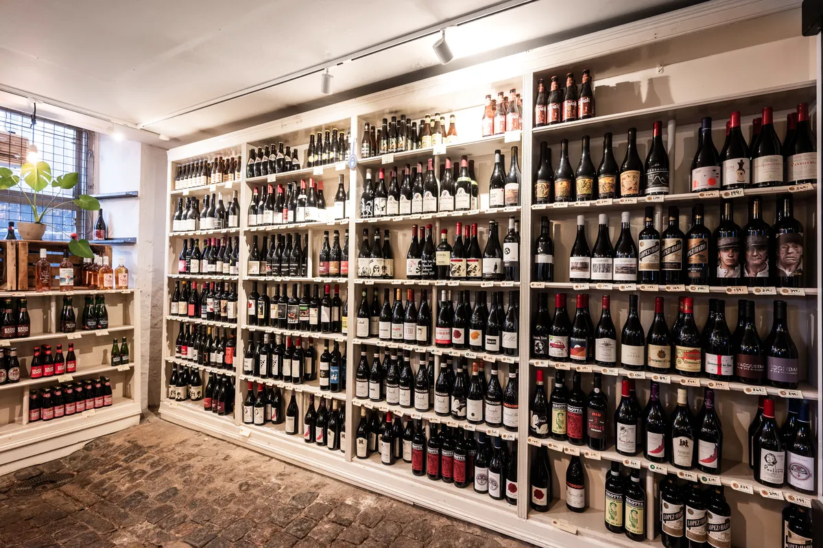 Butikslokaler med vinduer mod Gammel Strand. Store hvidfarvede hylder med sort etiketter og flere vinflasker. En plante i en potte til venstre.
