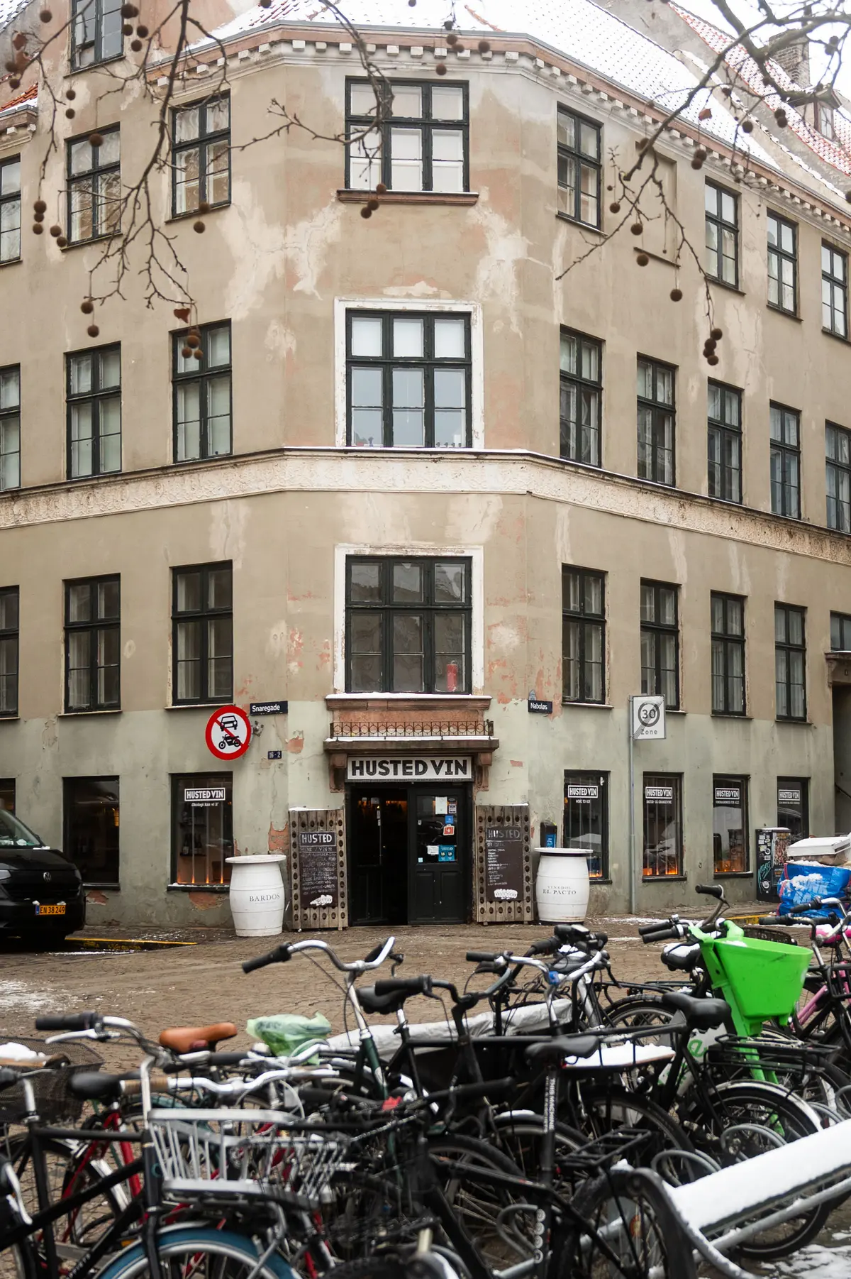 Mange cykler parkeret foran Husted Vin butik, der ligger i en gammel bygning med mange vinduer og nogle skilte på facaden