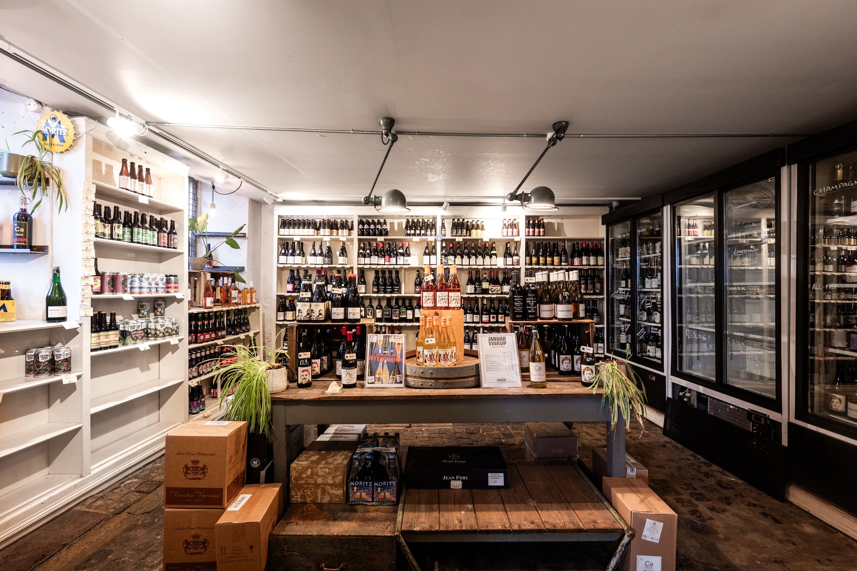 En butik med rækker af alkoholske drikkevarer og køleskabe, hvor borde og skuffer er fyldt med bokse og plantepotte