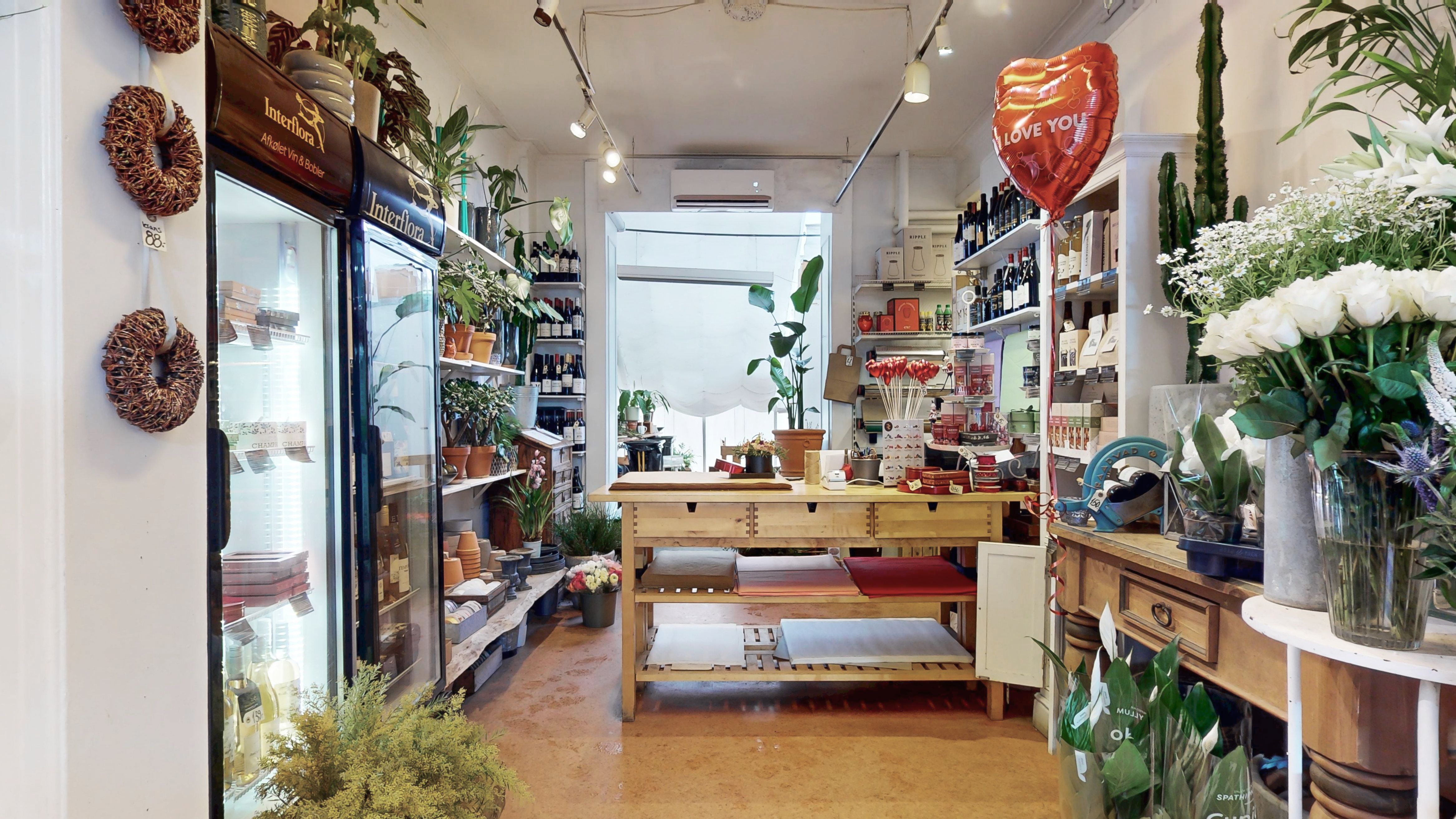 En vinbutik med vinduer og blomster samt vinduer med vinduer og plantehyller samt et bord med papiryder og et hjerteløn samt et vinglas og en vinduer med vinduer og blomster