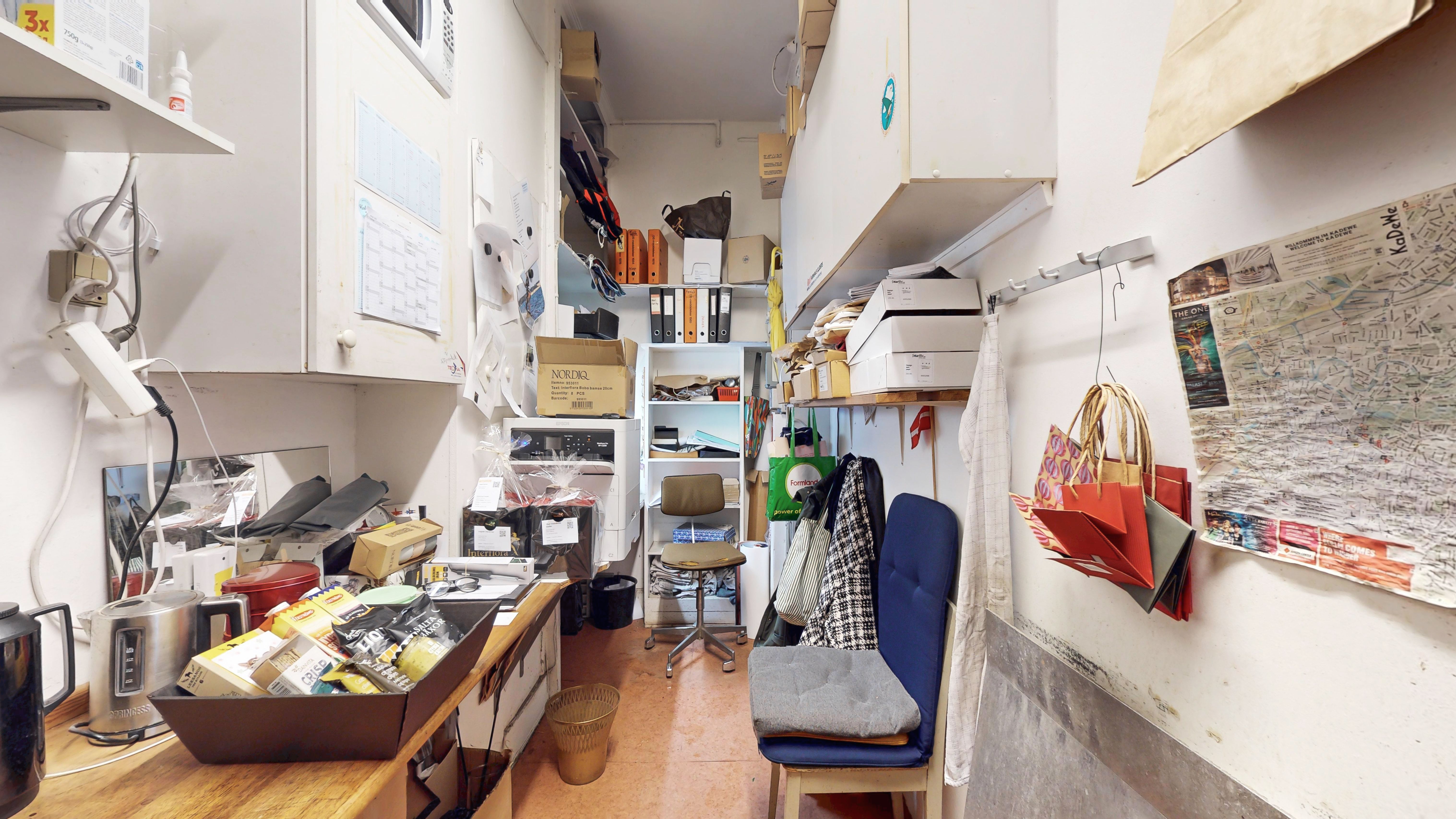 Alt-tekst: Remme på kontoret med papirkurve, møbler, hængekøkken og væghylder. Mange papirer og skraldekurv på loftet og et skraldespand på gulvet