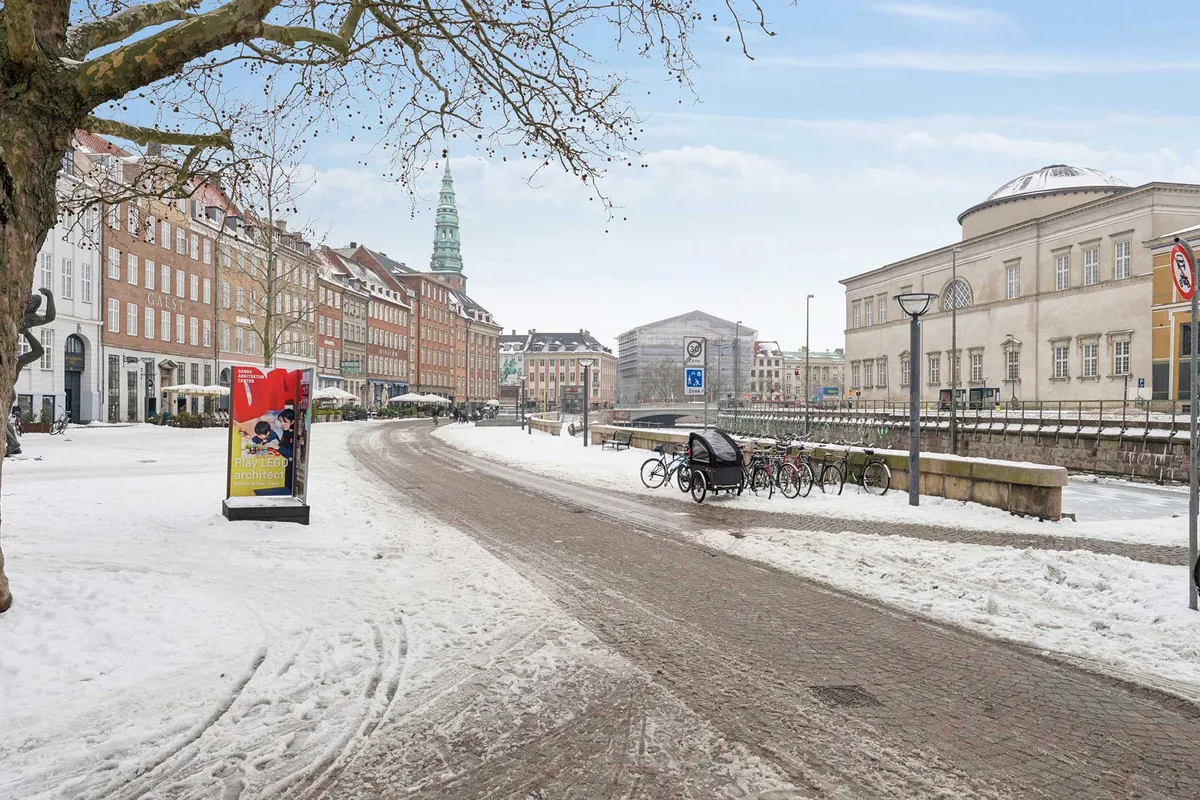 Sneede gade med snedækkede fortove, et reklameskilt for Lego, gamle bygninger med røde tag og hvide vinduer og flere cykler parkeret på siden af vejen