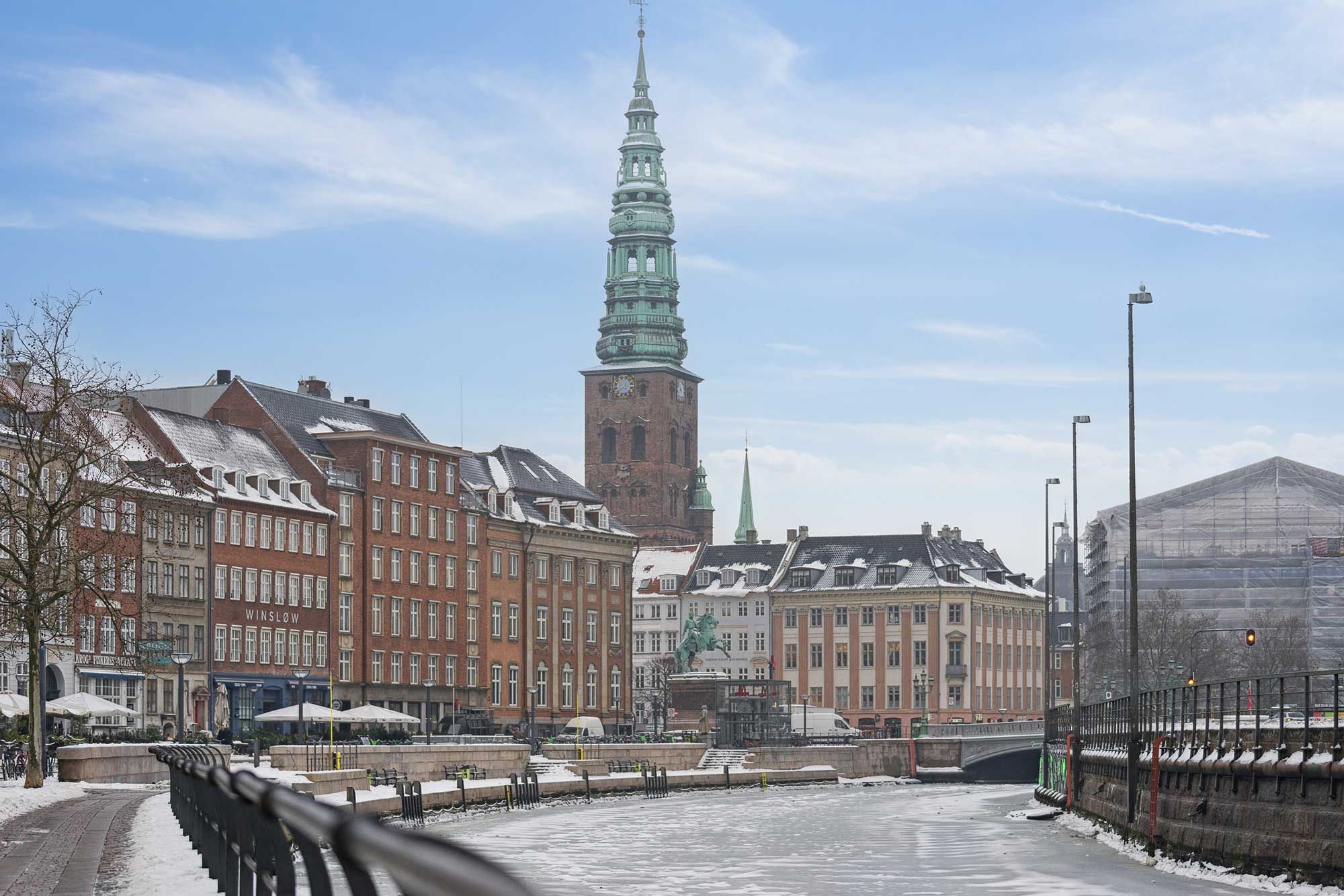 Lyse kontorlokale med bygning med grønt tag og søjlerne i baggrunden, der er dækket af sne, og der er et monument med statuer og søjler