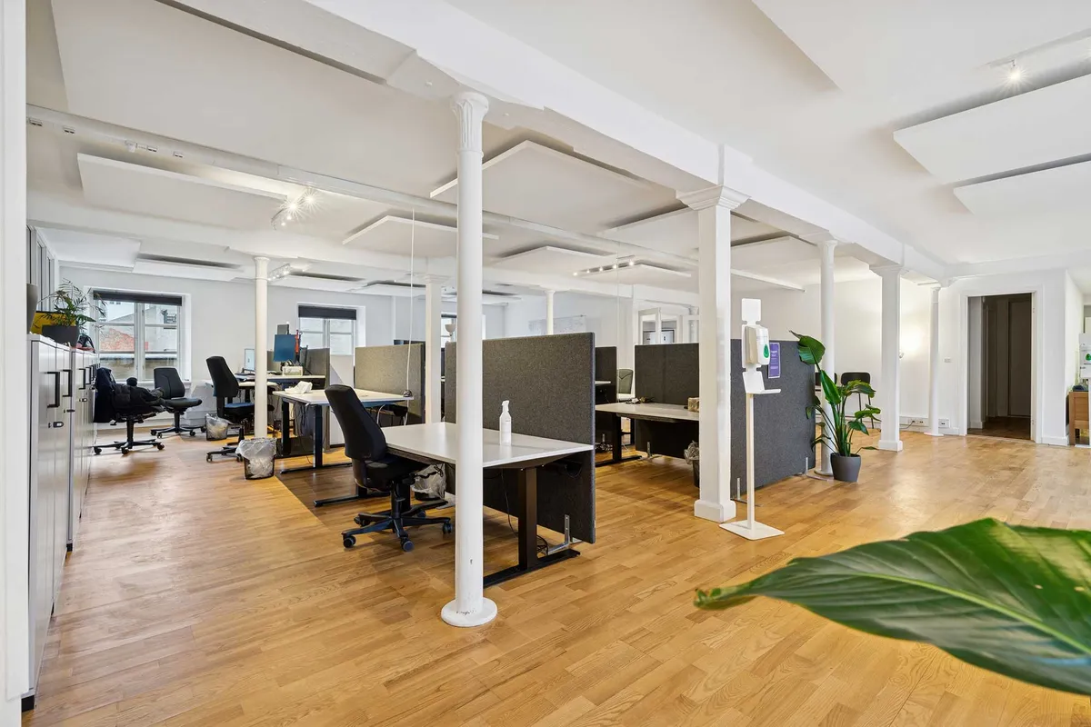 Et kontor med højloft, lyse vægge, og moderne møbler, der skaber et velkommende og inspirerende arbejdsmiljø, og kontoret er centralt beliggende i København