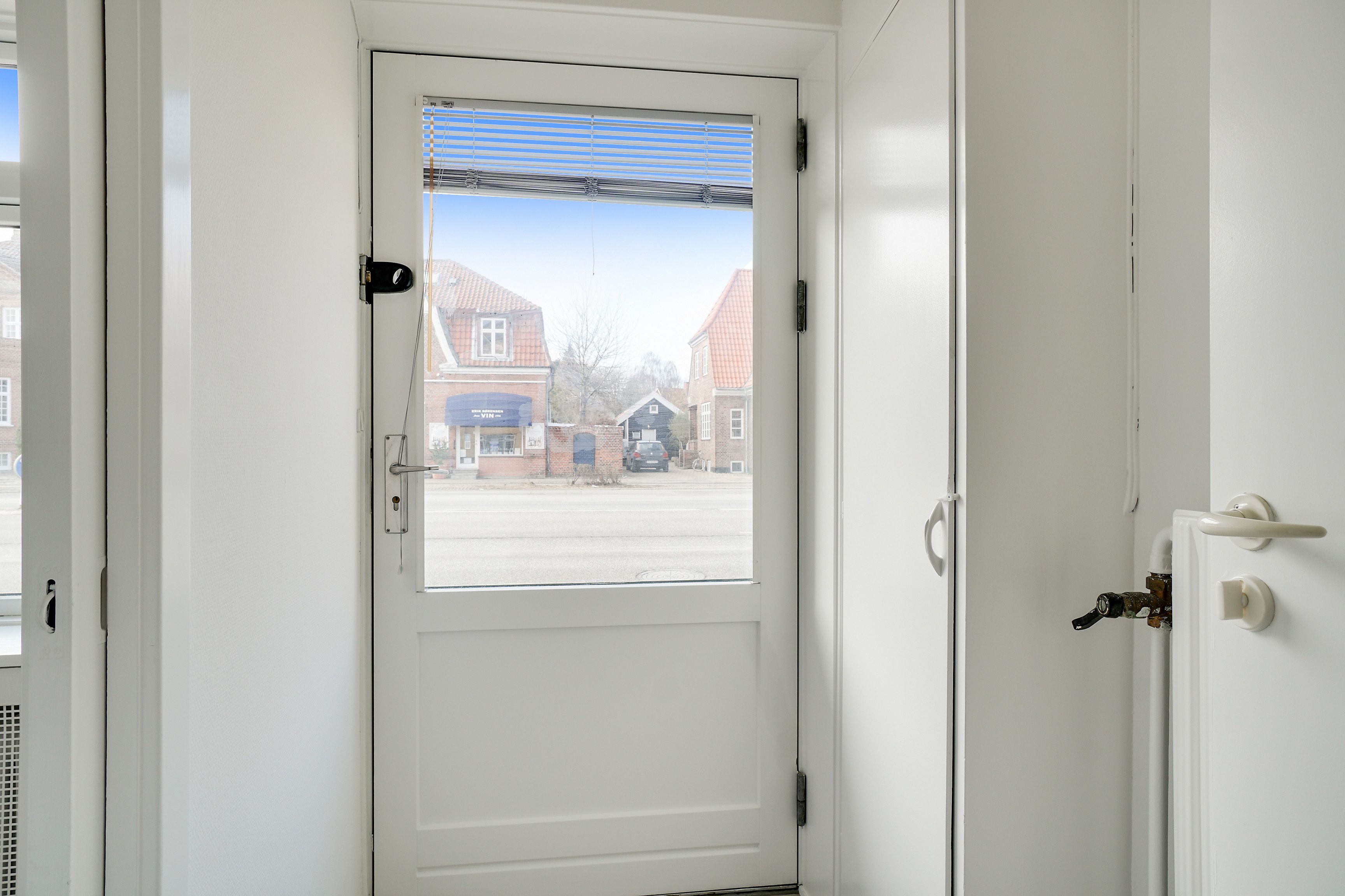 En hvid glasdør med et vindue og en lås, der vender ud mod en vej med bygninger og en parkeringsplads