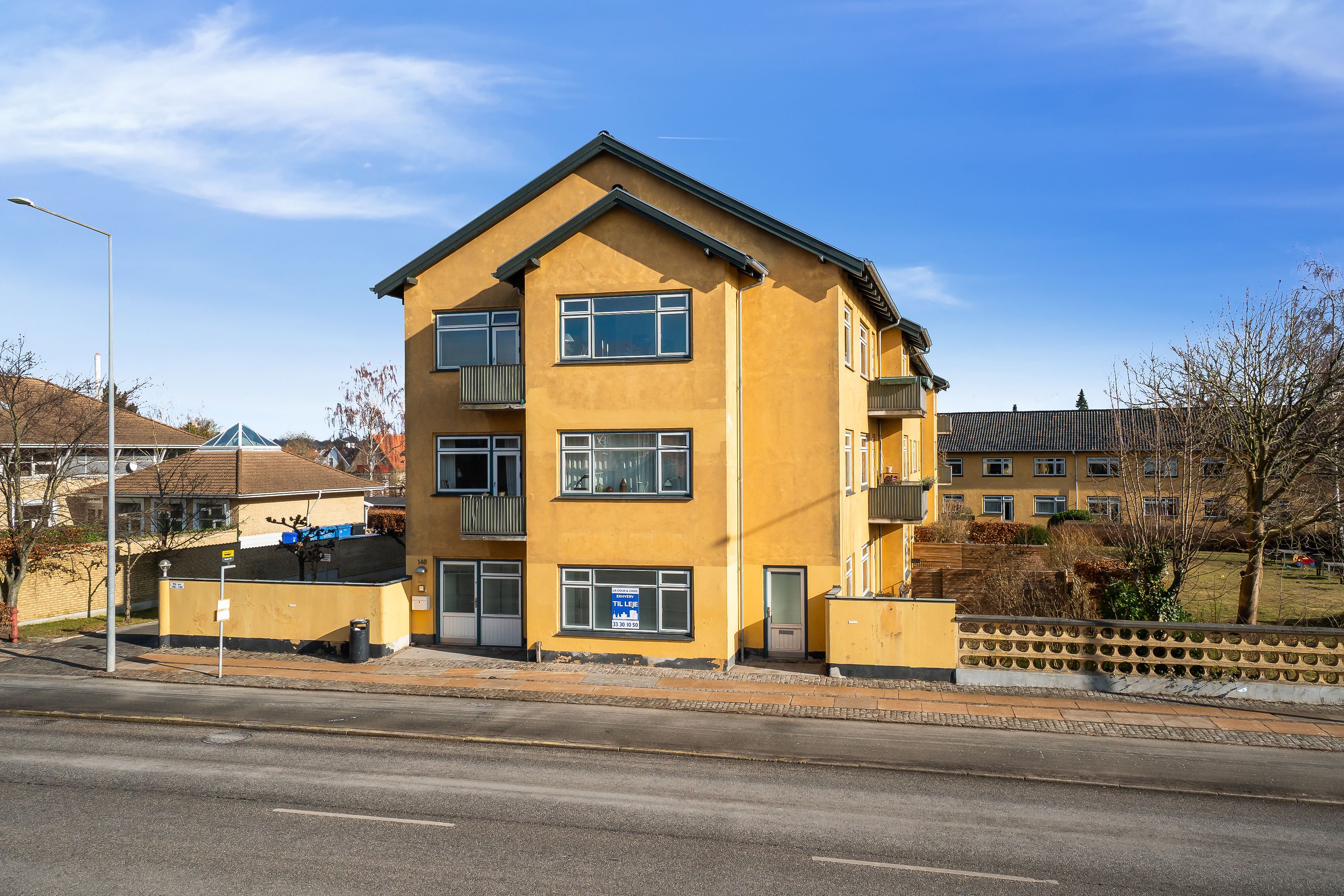 Kontor til leje på Bernstorffsvej 146 i Hellerup. Gult lejemål med balkoner og solrig udsigt. Området omgivet af grønne træer og buske.